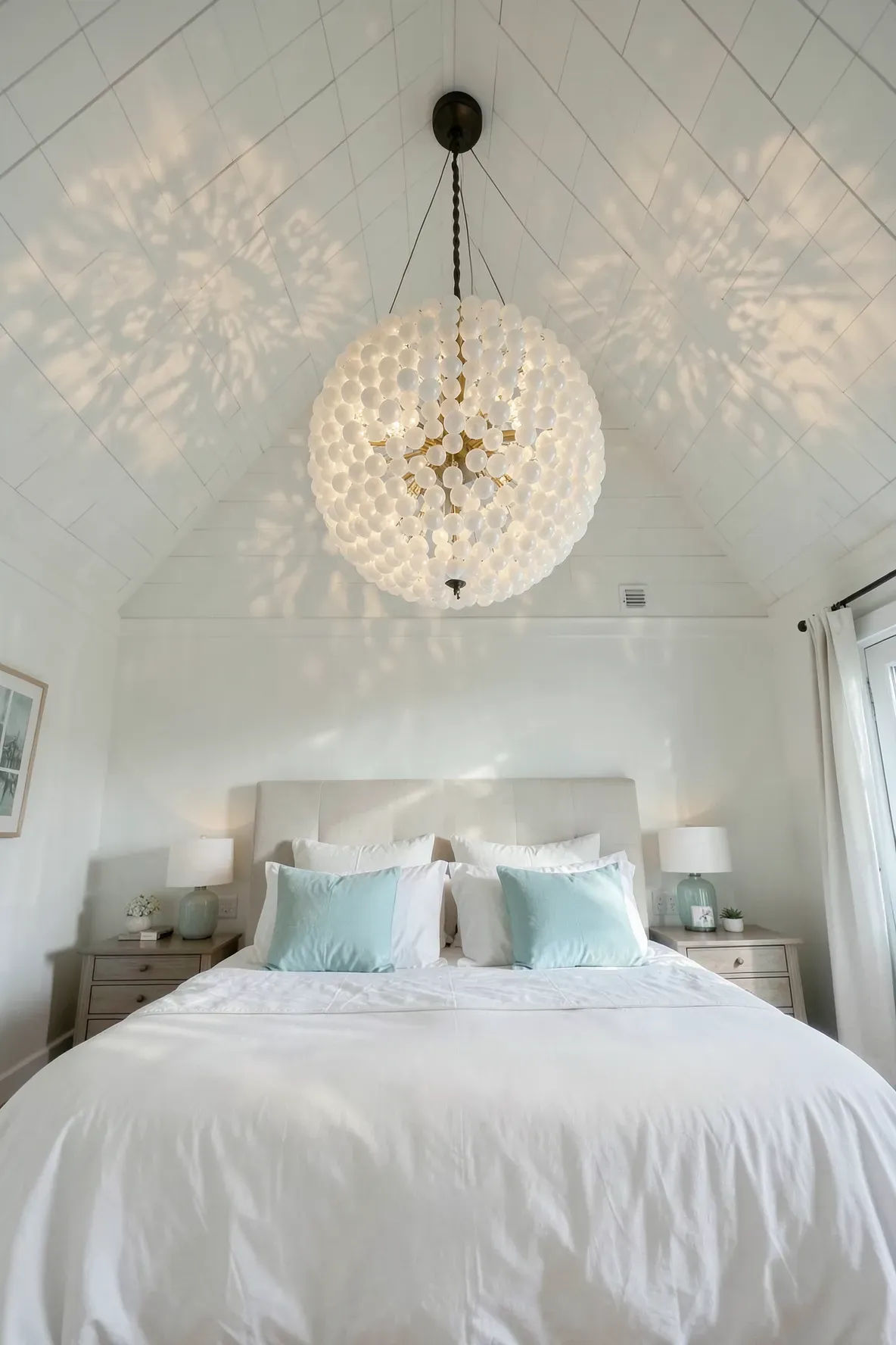 A sophisticated white sea glass beaded chandelier casting soft light in a breezy coastal bedroom.