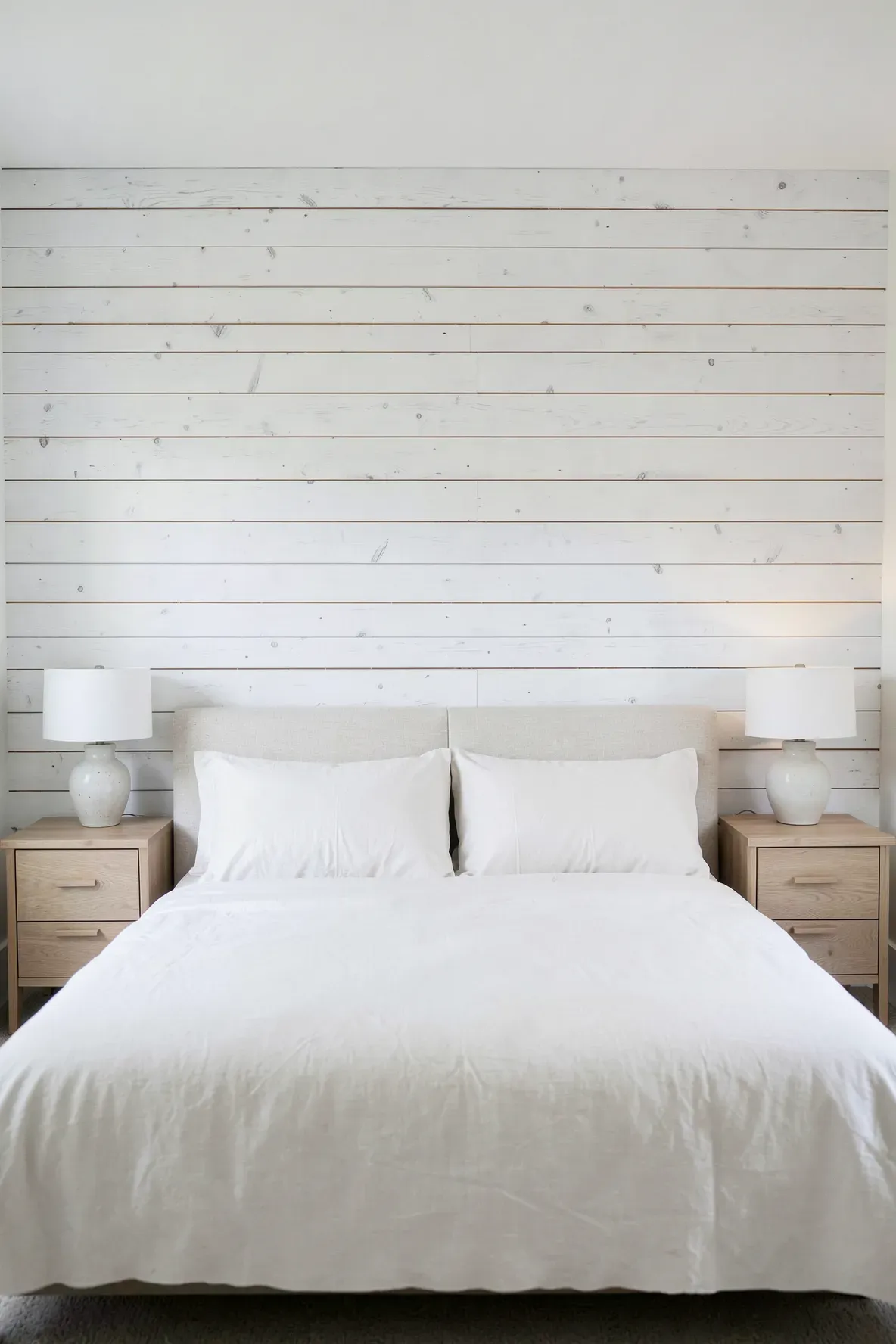 A bright bedroom featuring a horizontal whitewashed shiplap accent wall behind a soft linen bed.
