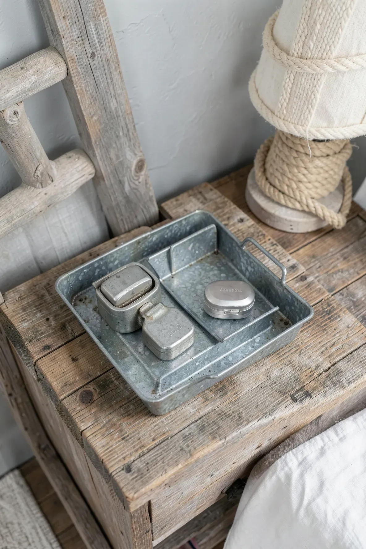 A rustic galvanized metal tray on a wooden nightstand holding glasses and a watch.
