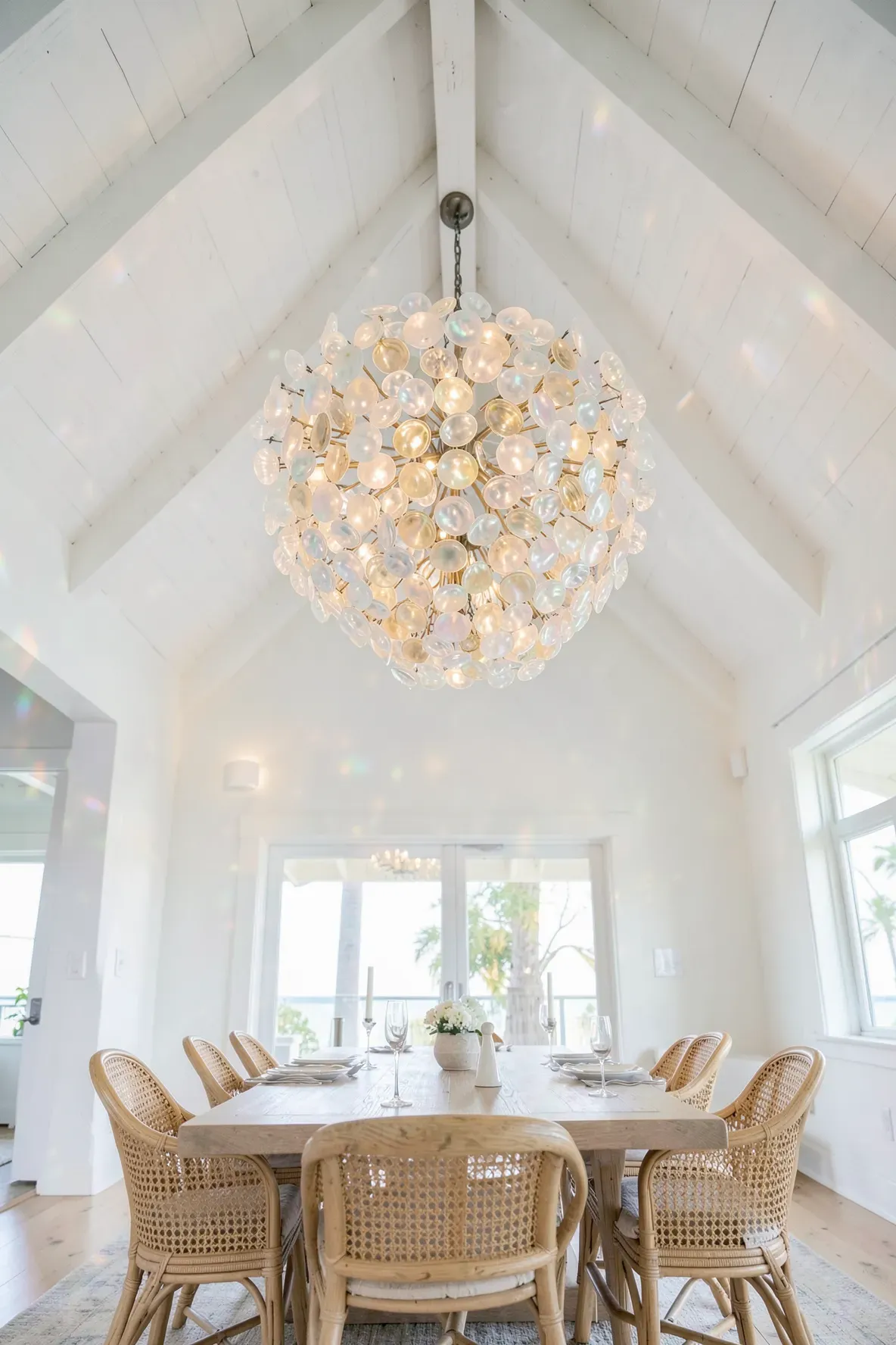 A tiered capiz shell chandelier hanging from a white vaulted ceiling in a coastal dining room.