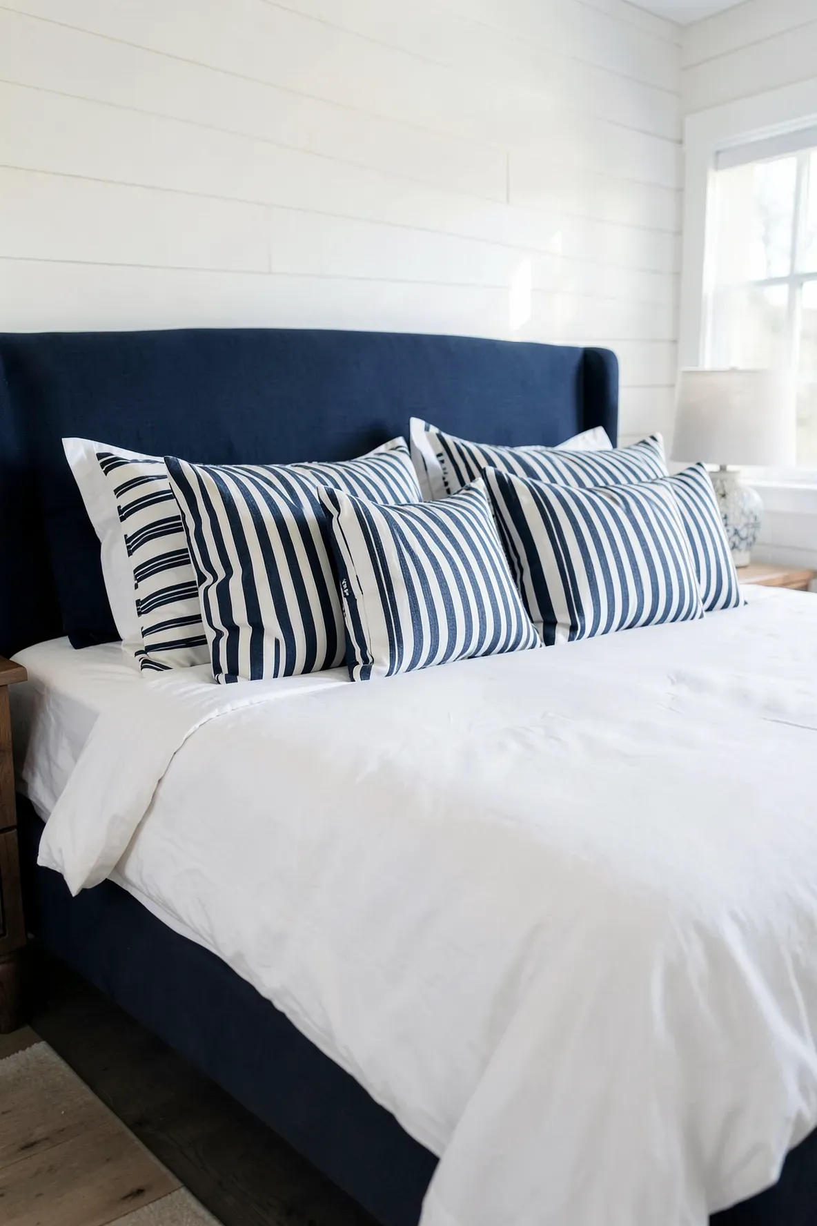 Navy and white striped throw pillows arranged on a white bed in a nautical-themed room.