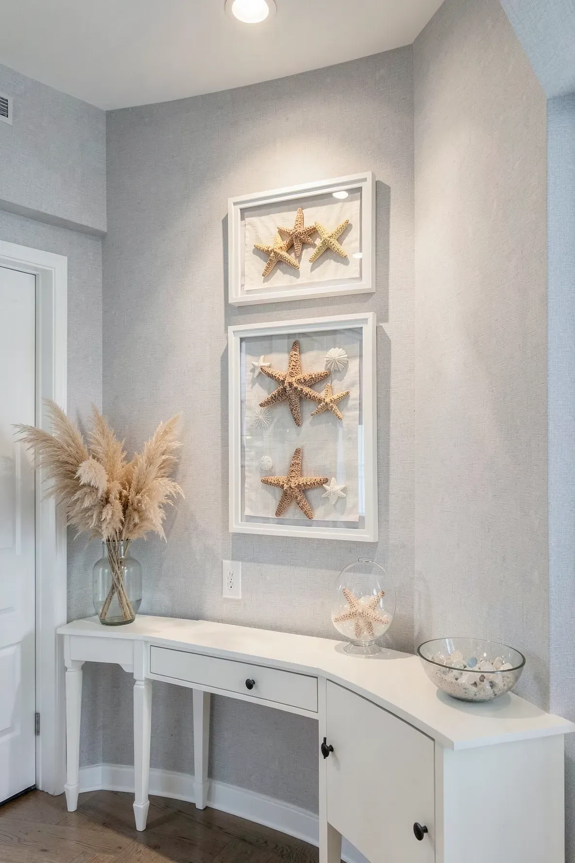 Starfish and sand dollars displayed in white shadow boxes on a wall in a coastal entryway.