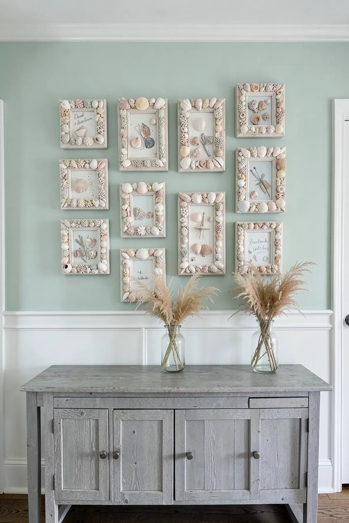 A collection of seashell-encrusted picture frames displayed on a seafoam green wall in a coastal home.