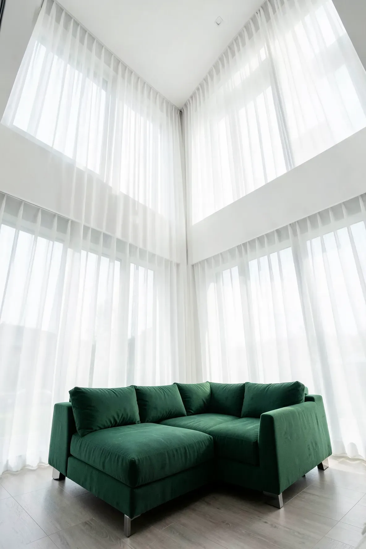 A green sofa in front of tall, airy white sheer curtains with bright natural light.