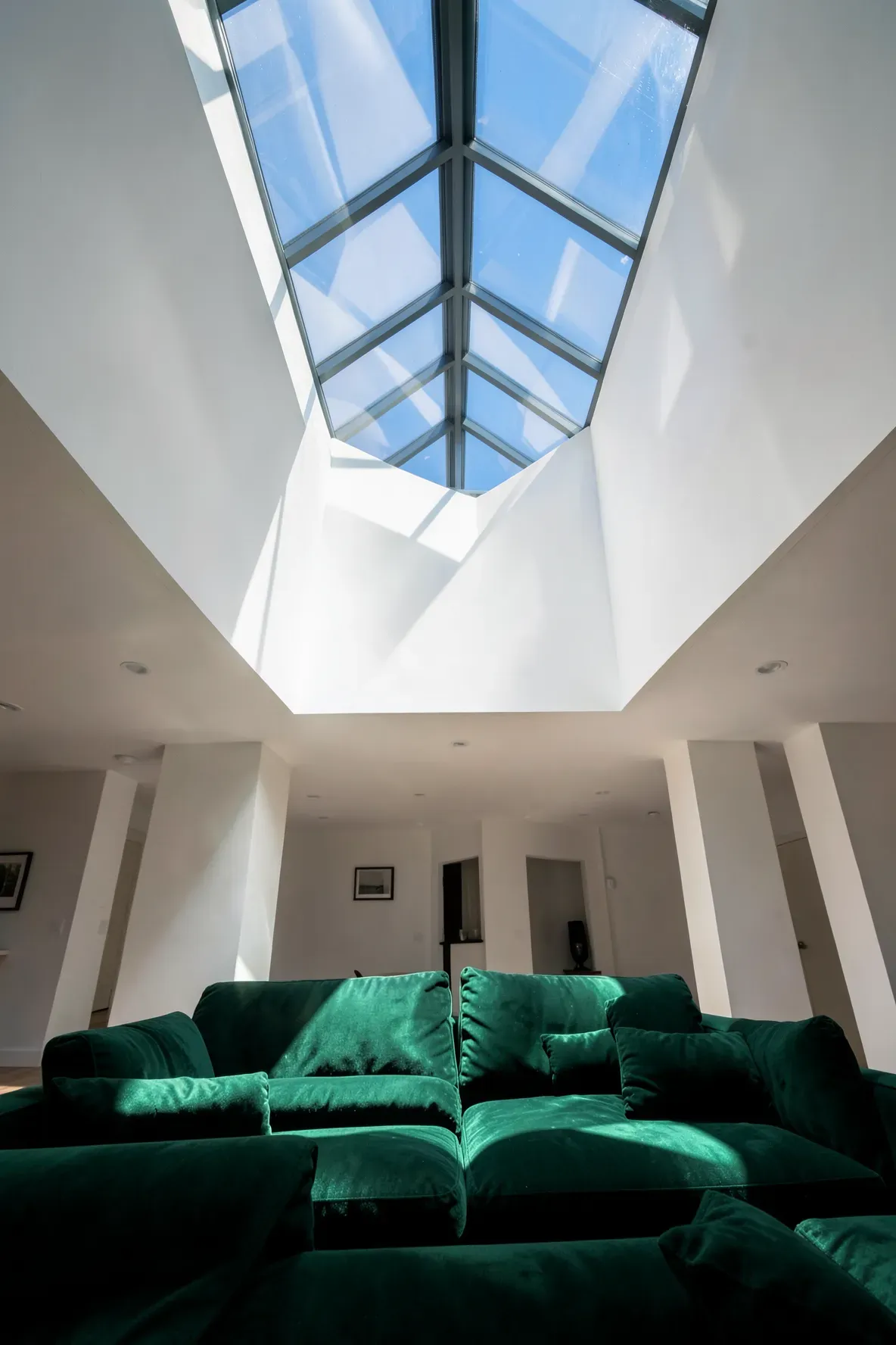 A vibrant green sofa bathed in bright natural light coming from a large glass skylight overhead.