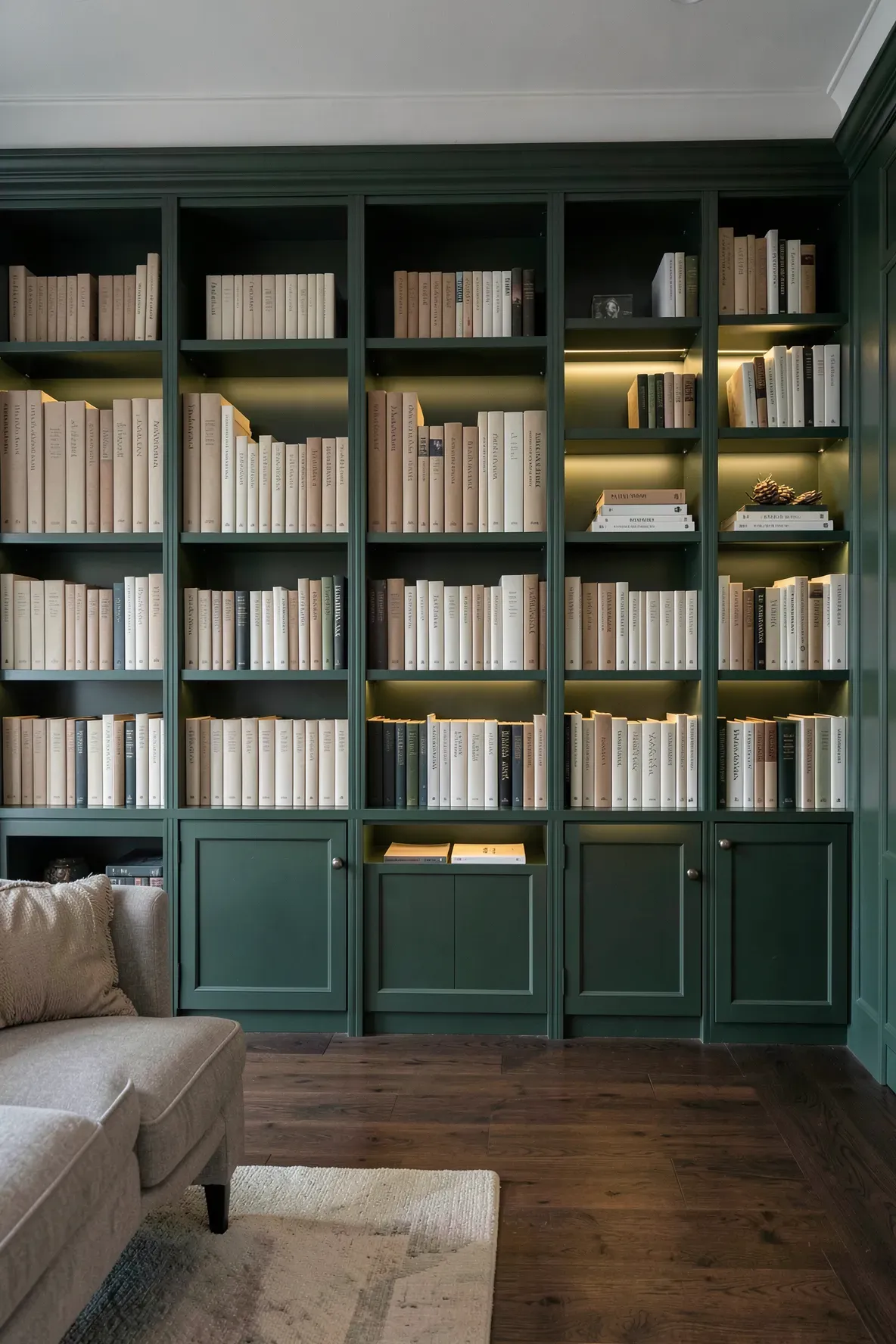 A deep juniper green bookshelf with neutral-colored books in a stylishly designed living room.