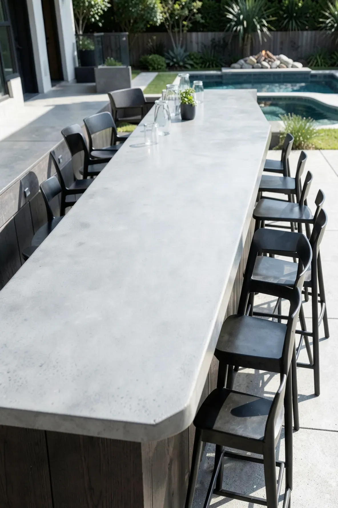 A modern outdoor bar with a polished grey concrete countertop and industrial-style seating.