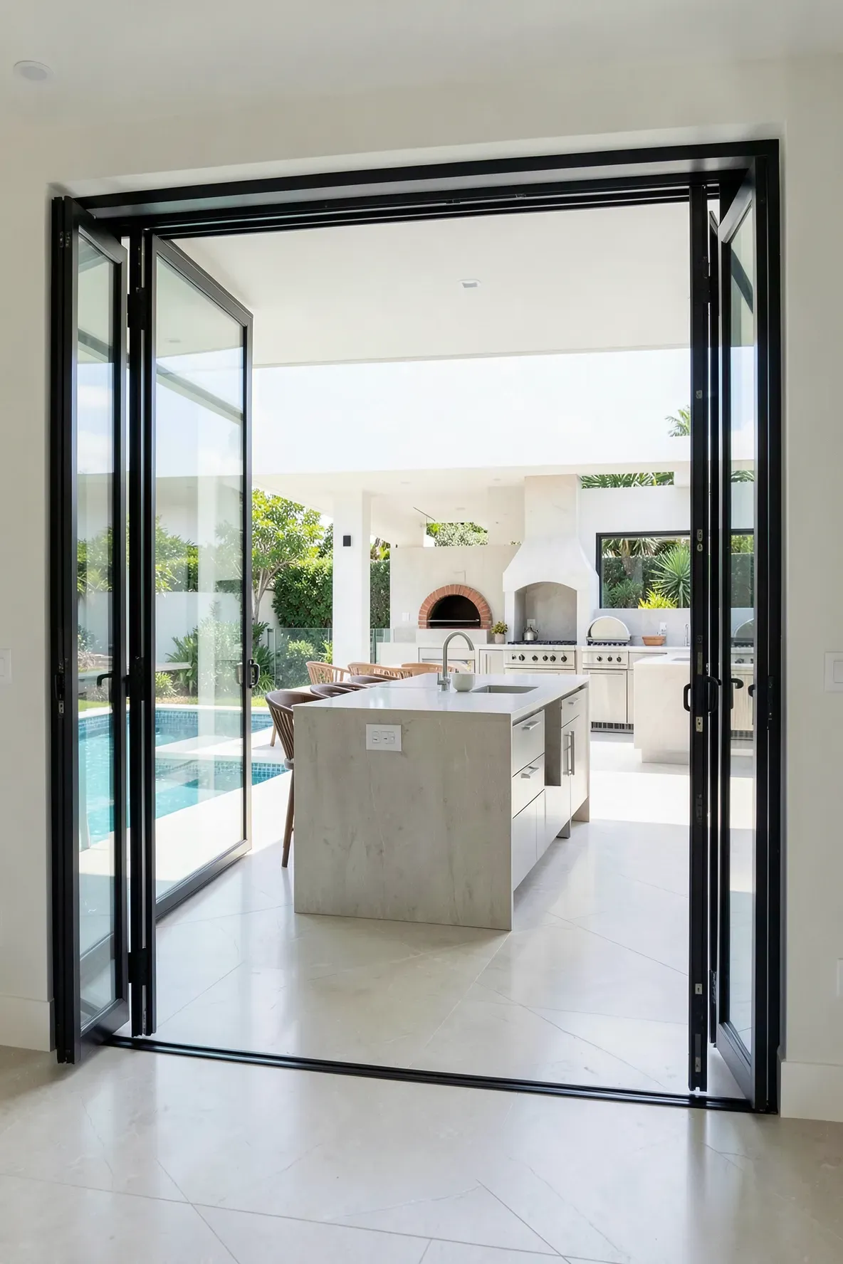 Large folding glass doors opened wide to connect an indoor kitchen with an outdoor patio kitchen.