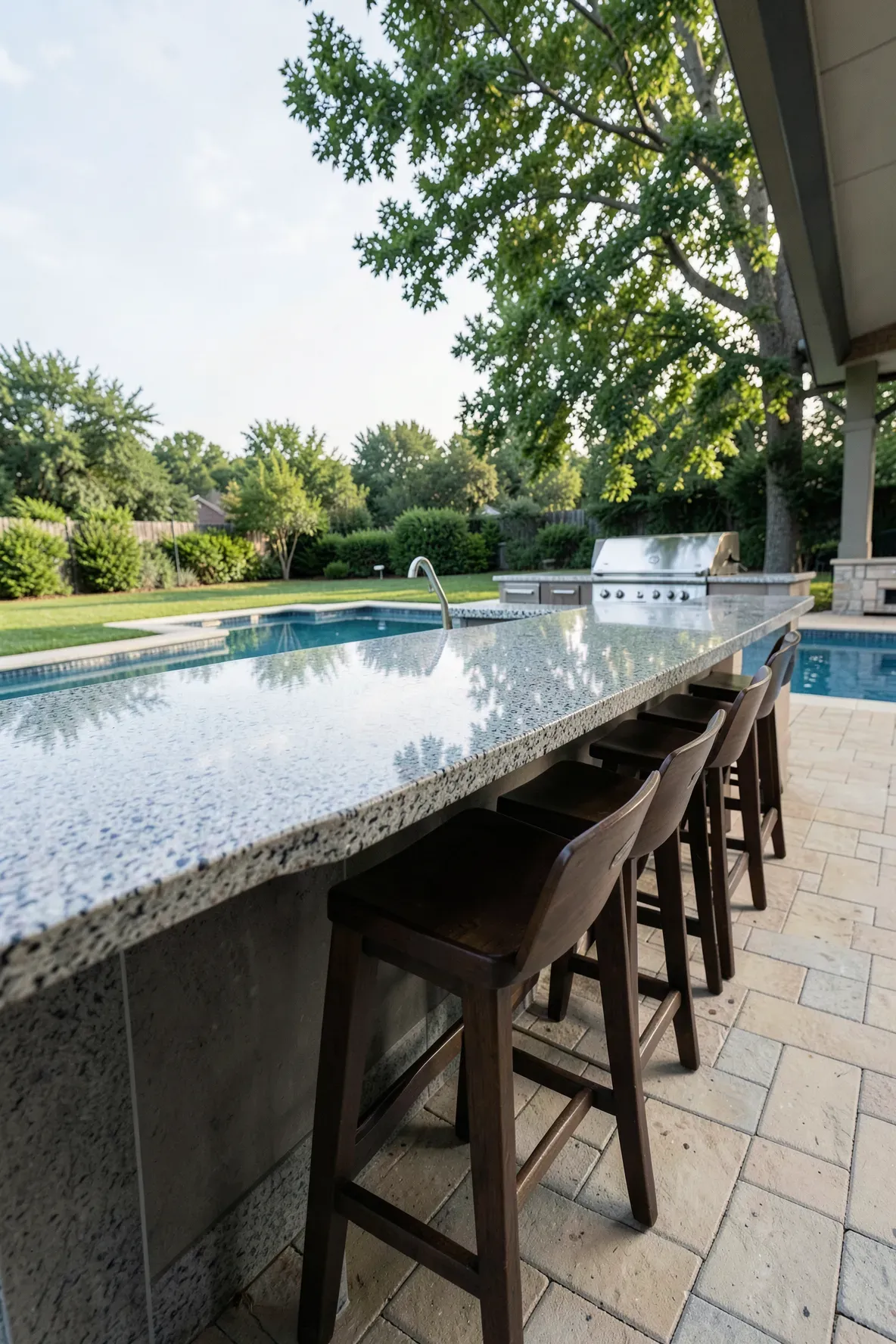 A wide granite outdoor kitchen counter with a dining overhang and stylish bar stools.