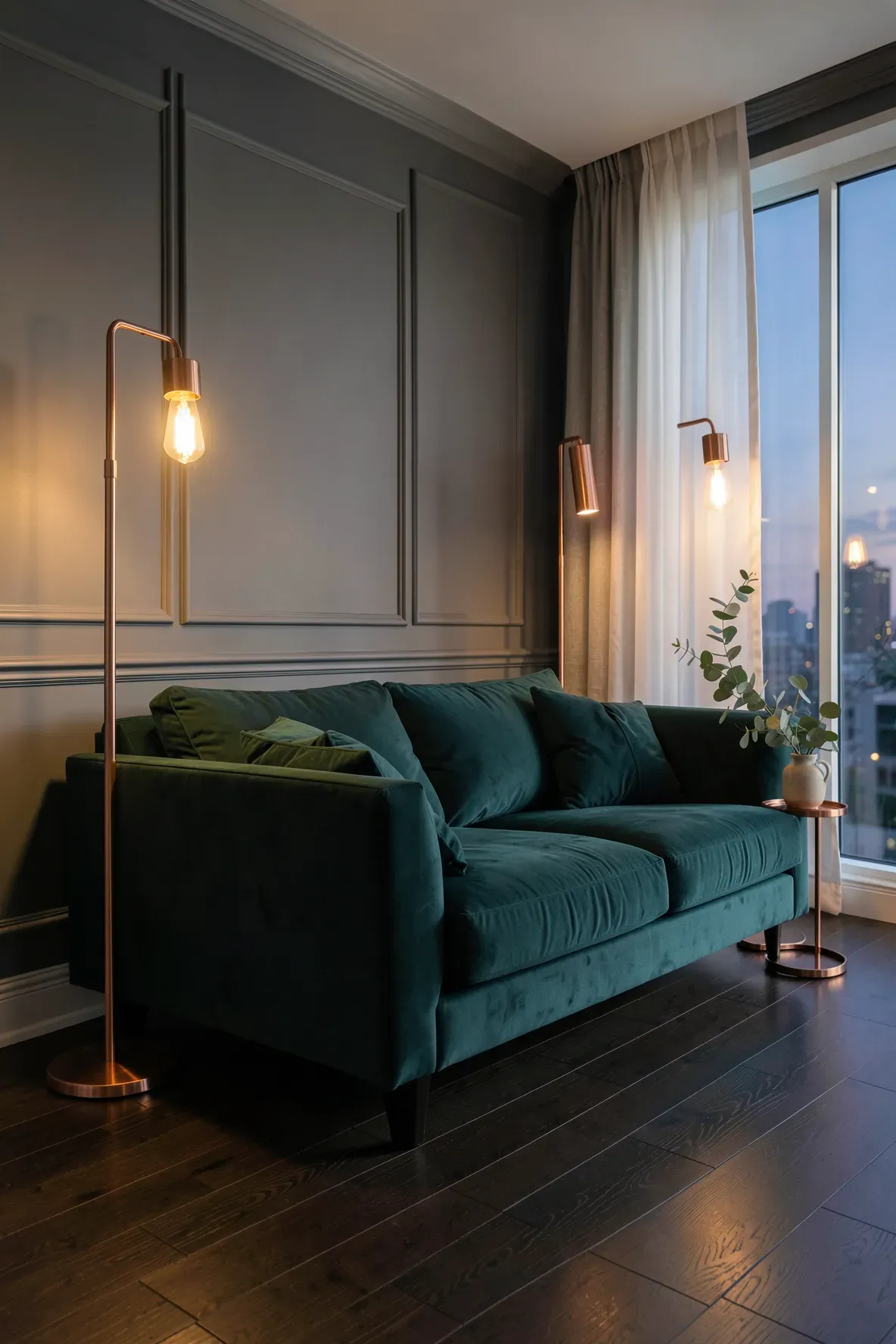 A dark teal-green velvet sofa in a modern living room illuminated by warm copper floor lamps.