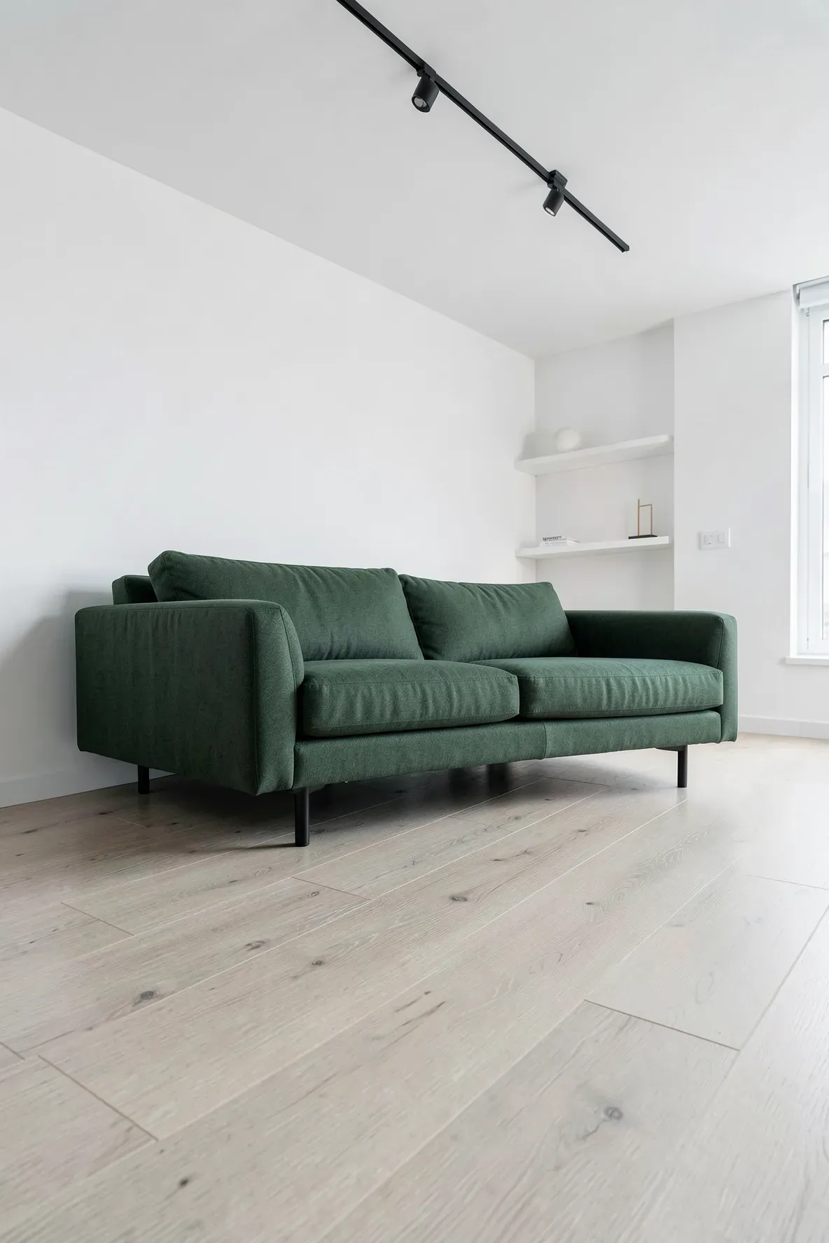 A dark pine green couch on light ash wood floors in a minimalist white living room.