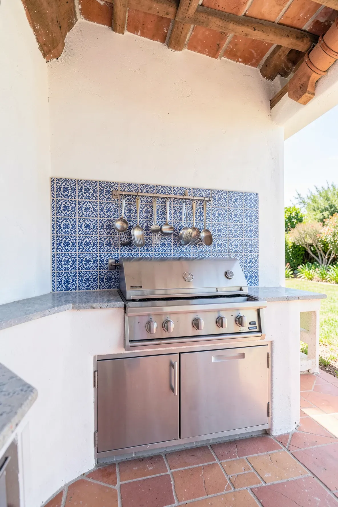 A blue and white patterned tile backsplash with a magnetic rack holding grilling tools in an outdoor kitchen.