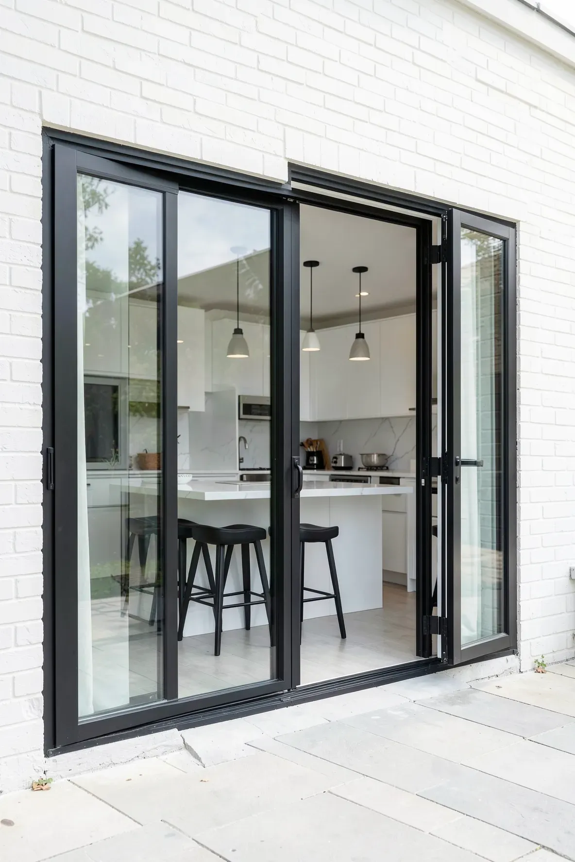 A black bifold window open to create a pass-through bar from a white kitchen to a patio.