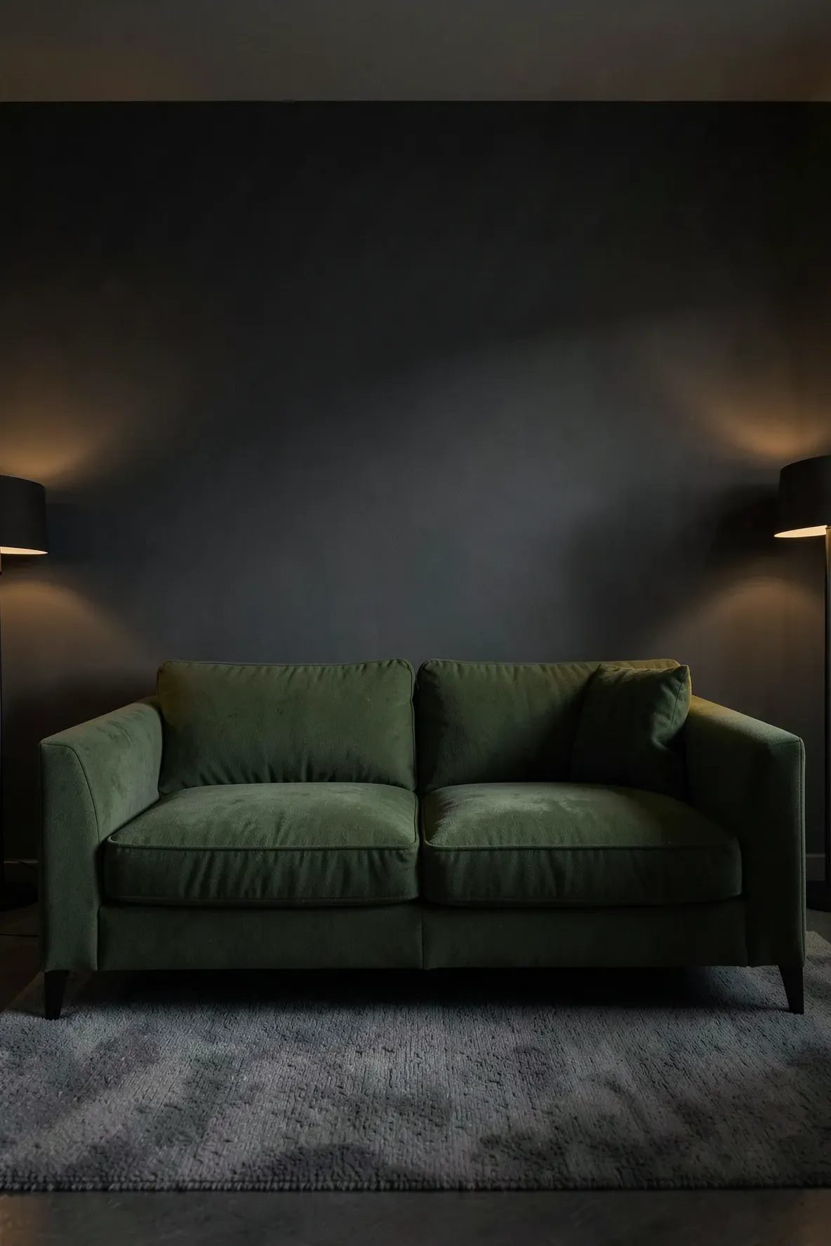 A moss green sofa against a dark charcoal gray wall in a moody, sophisticated living room.