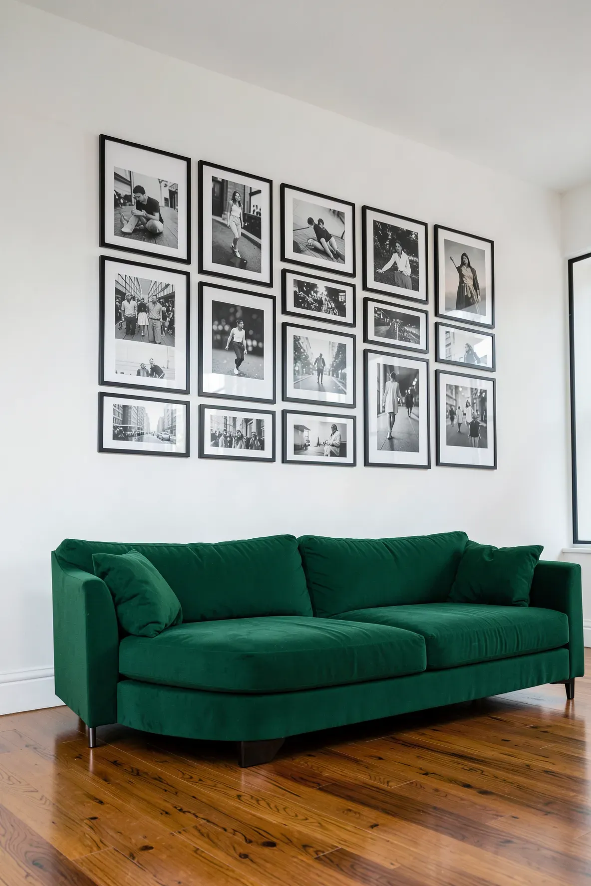 A green sofa sitting under a professional gallery wall of black and white framed photos.