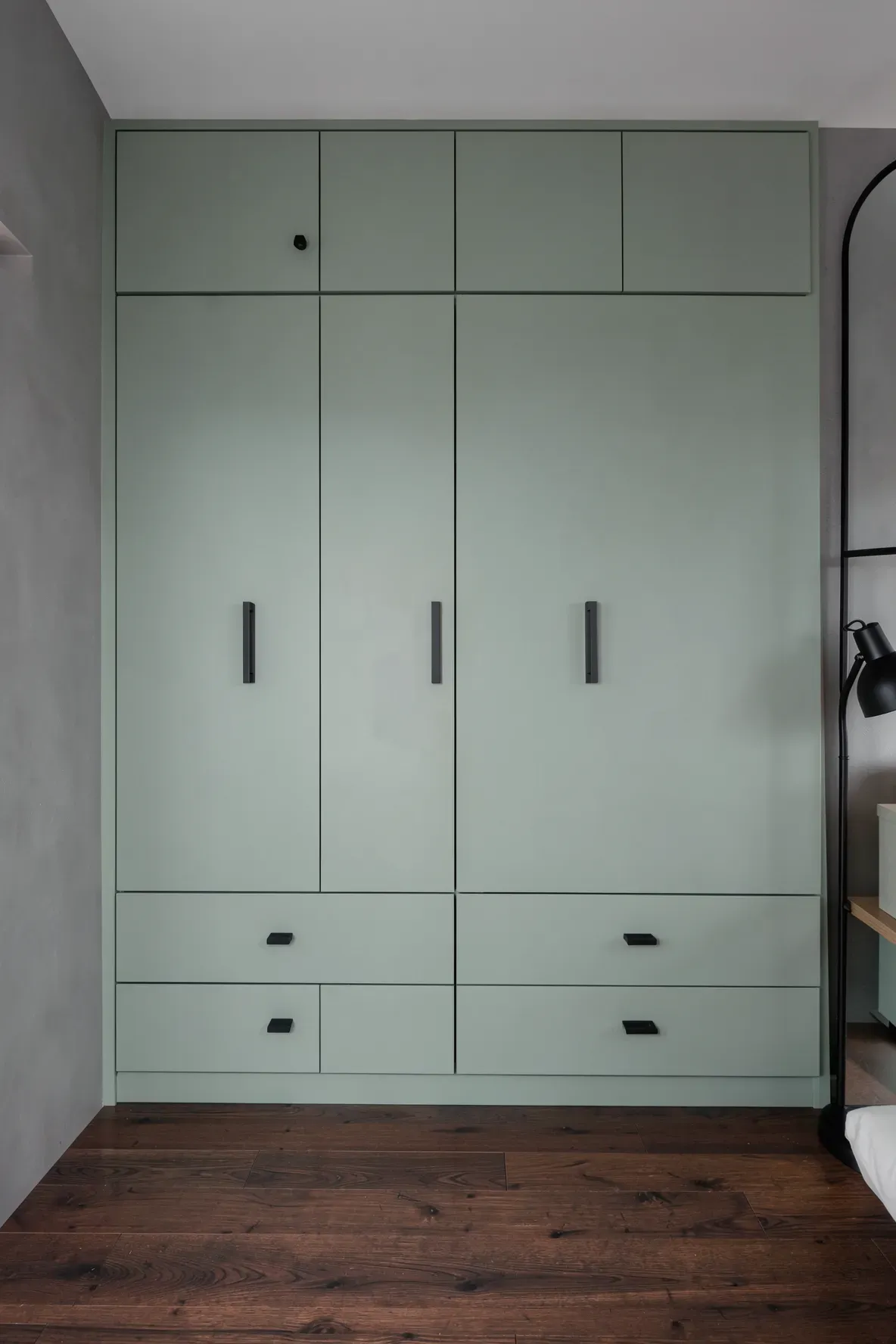 Sage green bedroom cabinets featuring modern matte black handles and a clean, minimalist design.