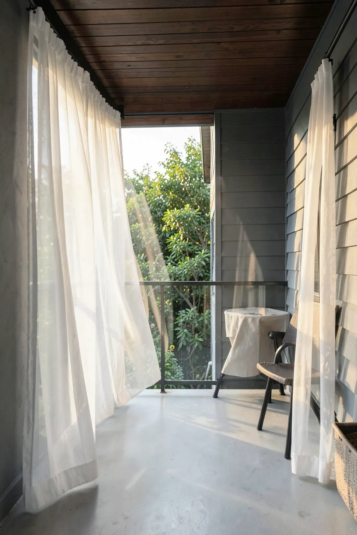 Sheer white curtains blowing in the breeze on a sunny, modern small outdoor patio.