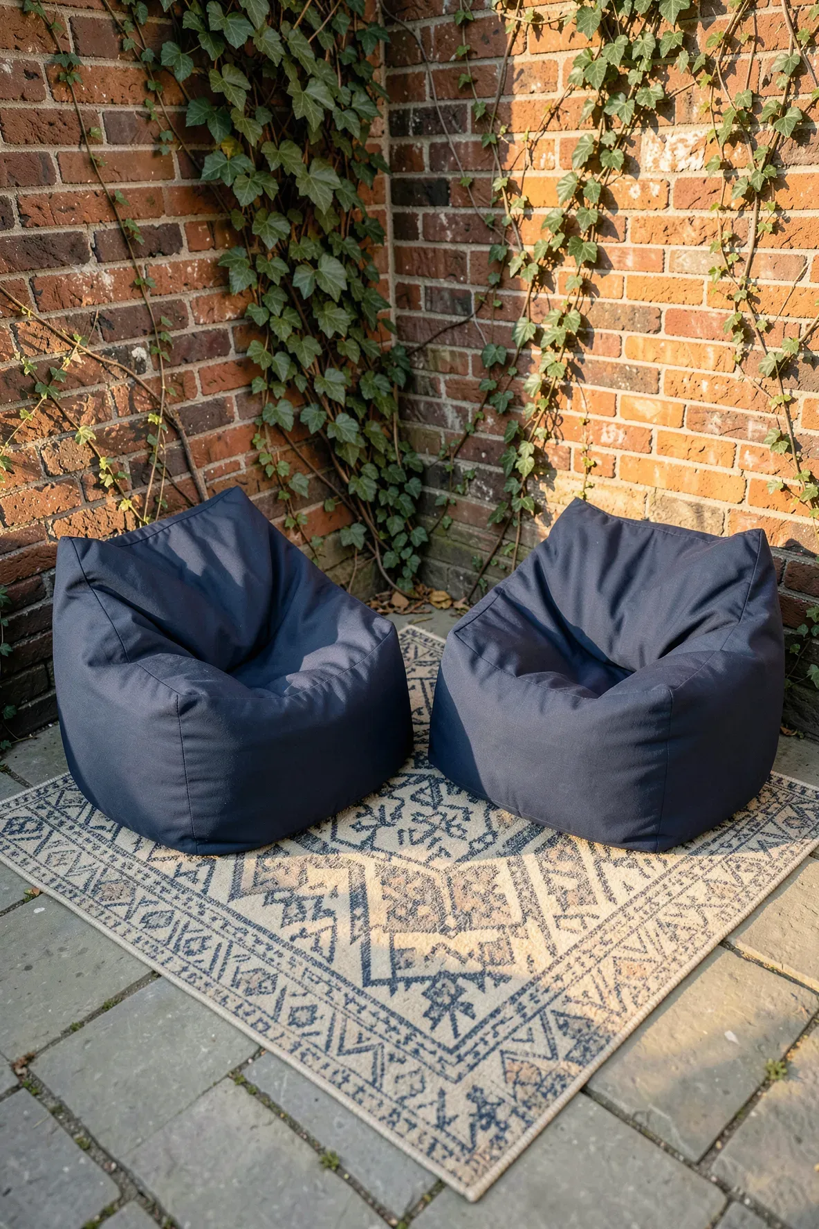 Two navy blue marine-grade bean bag loungers on a brick patio with a patterned rug.