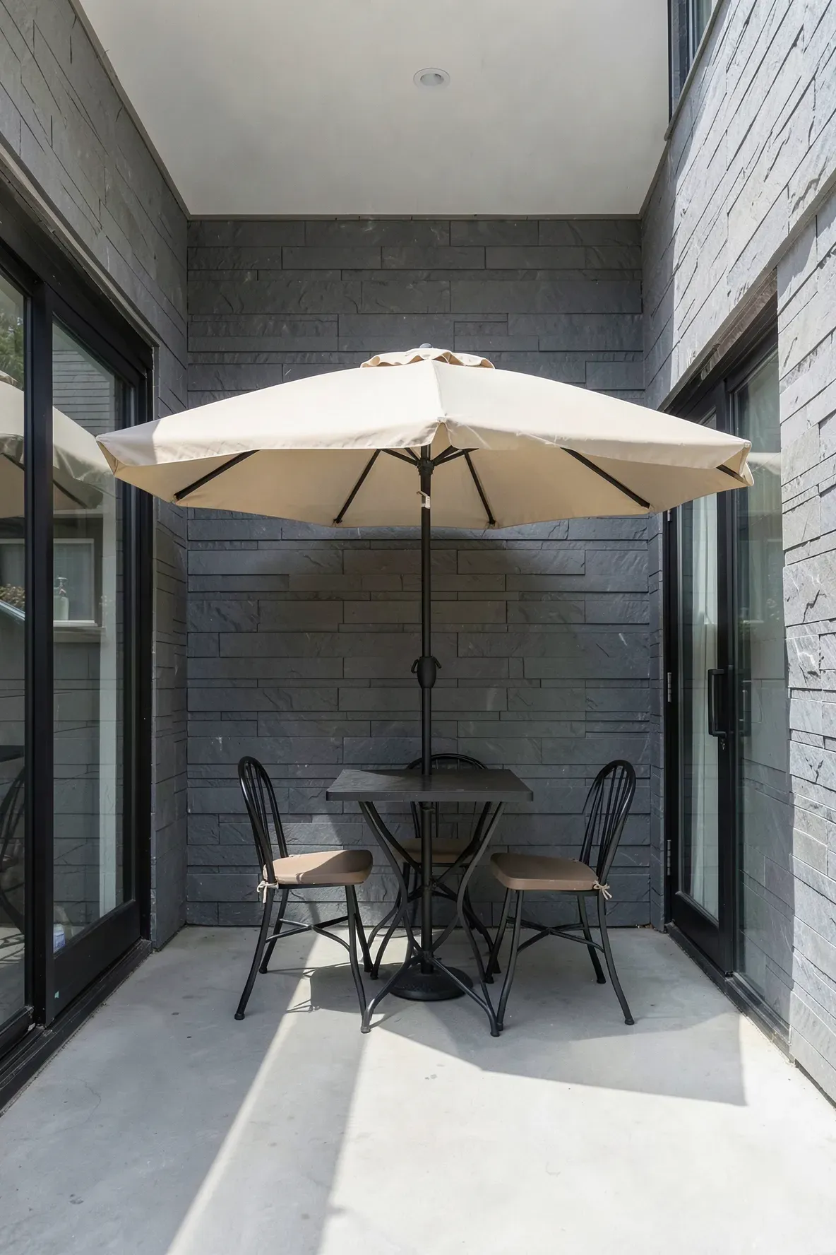 A sand-colored half-moon umbrella standing flush against a wall over a small patio table.
