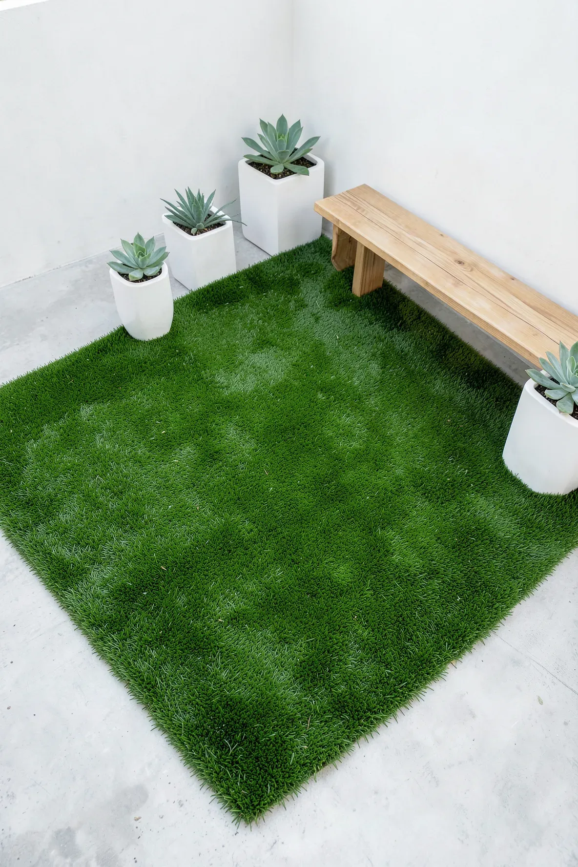 A bright green artificial grass patch covering a concrete patio floor with modern white planters.