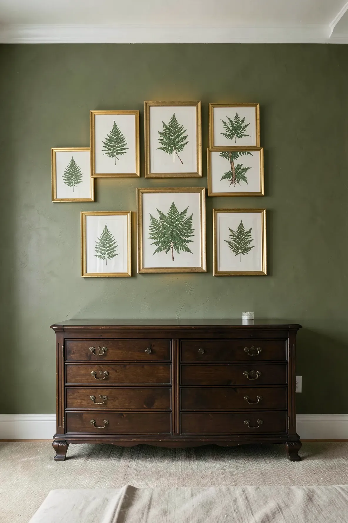 Botanical fern prints in ornate gold frames mounted on an olive green bedroom wall.