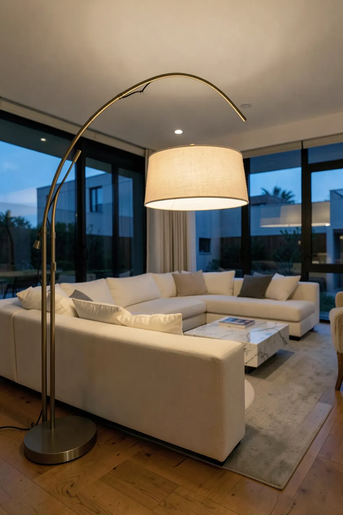 A large arch floor lamp with a warm shade hanging over a cream sectional sofa in a modern open-plan living room.