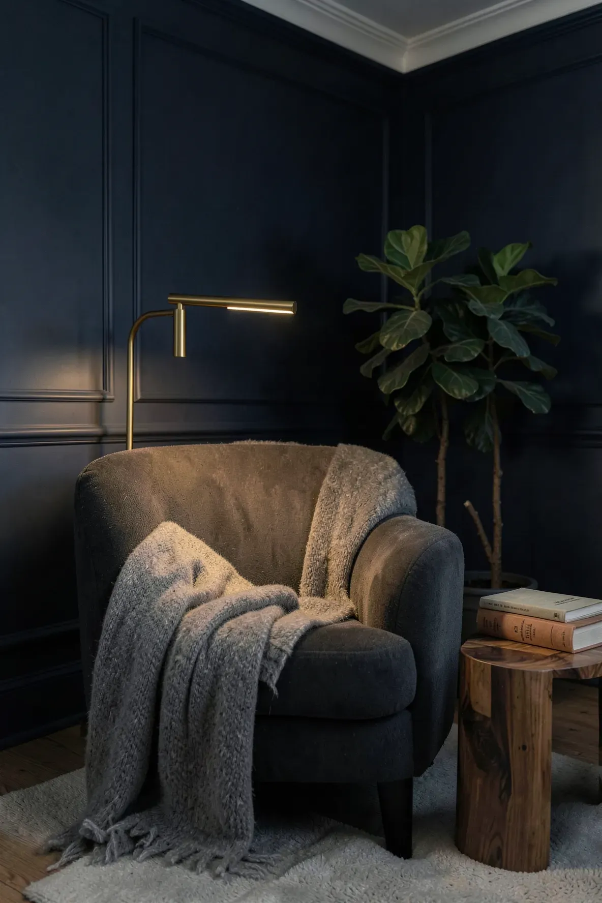 A slim brass pharmacy lamp illuminates a cozy grey reading chair in a dim, elegant living room.