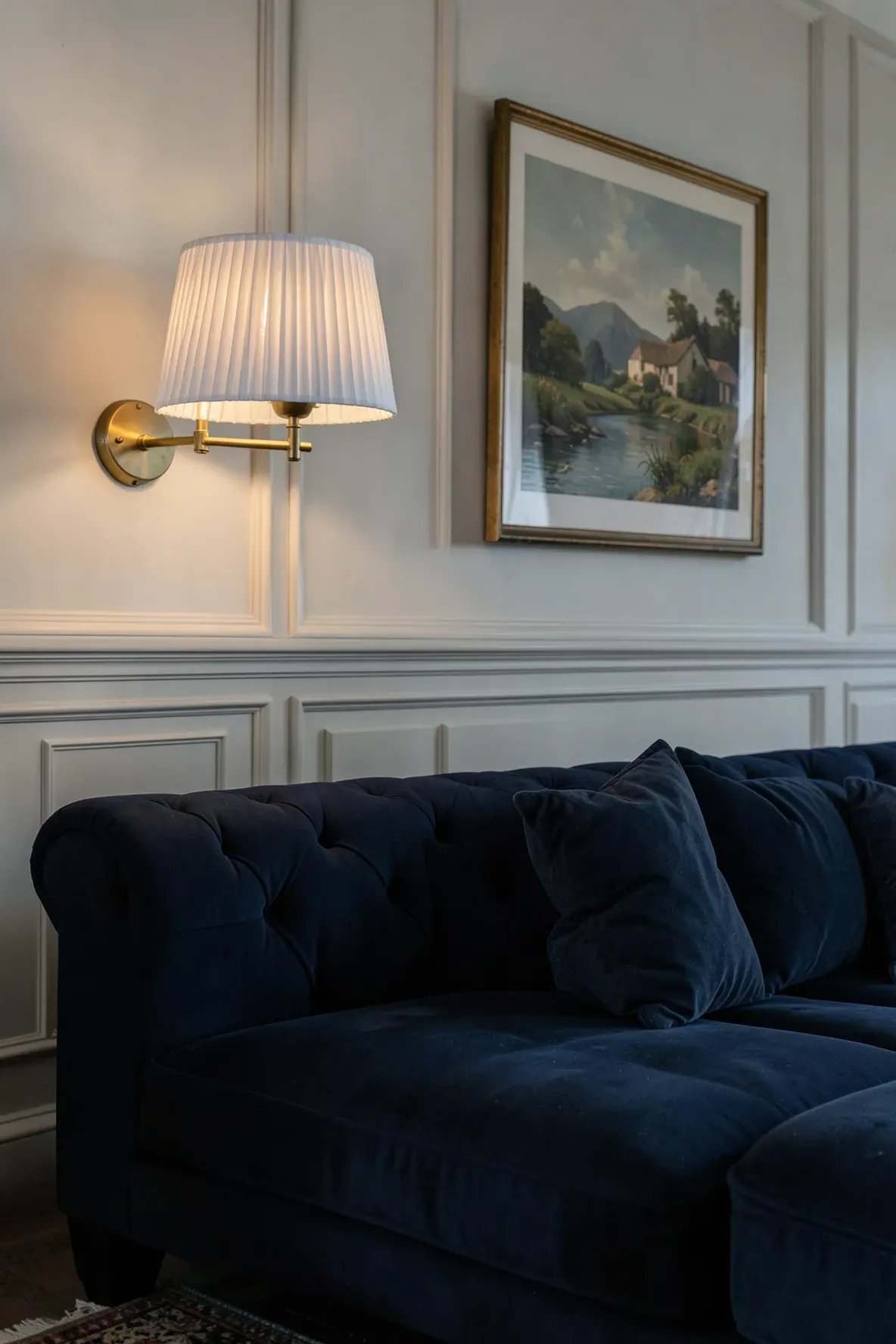 A brass swing-arm lamp with a pleated shade mounted on a wall above a blue sofa in a classic room.