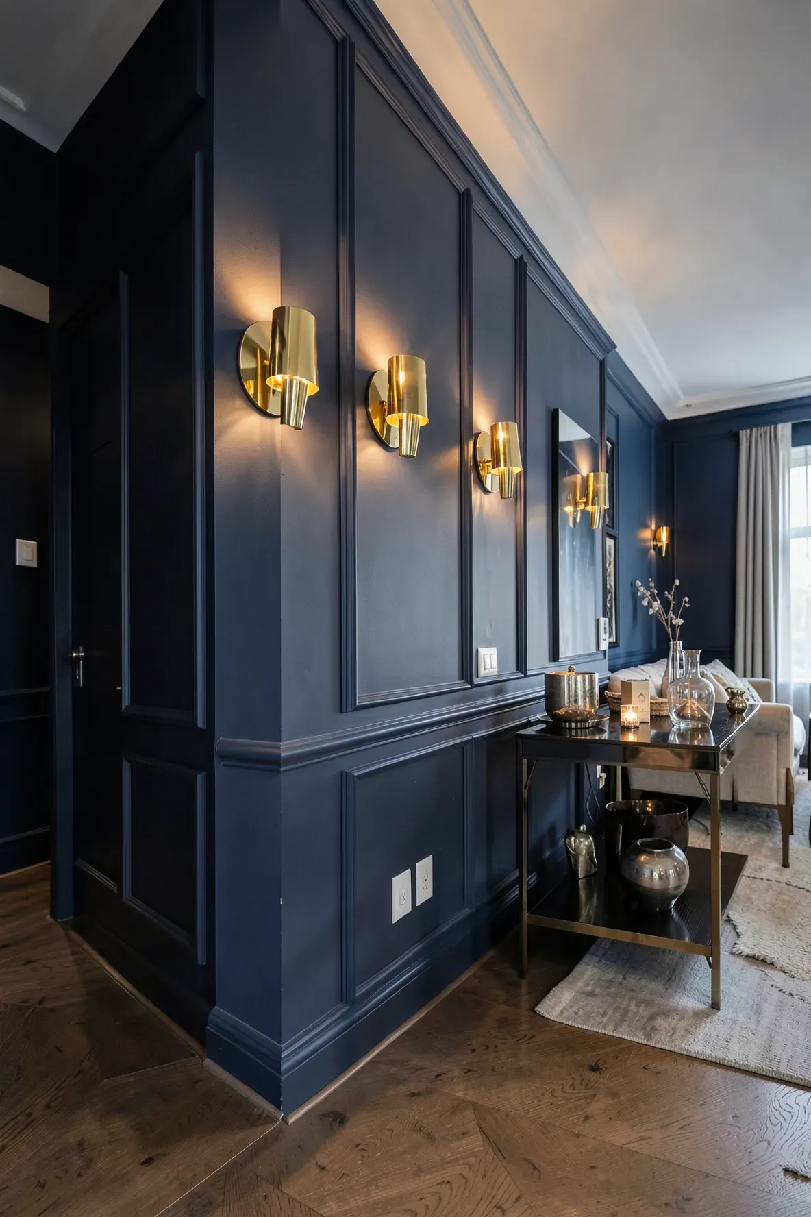 Polished brass wall sconces reflecting warm light against a dark blue living room wall.
