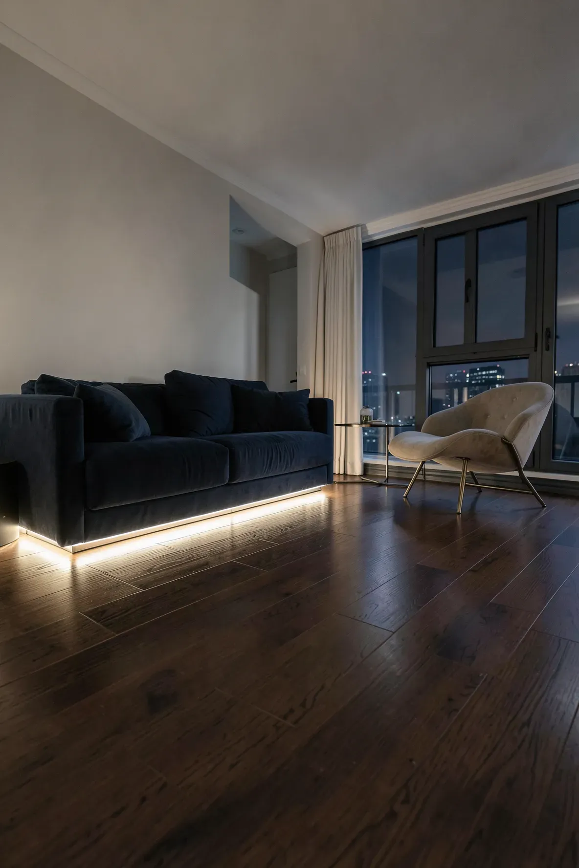 A dark living room with warm LED strips glowing along the baseboards and under the furniture.
