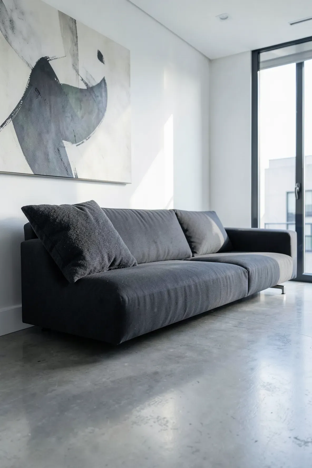 A modern charcoal sofa with a single oversized wool pillow in the corner within a minimalist room.