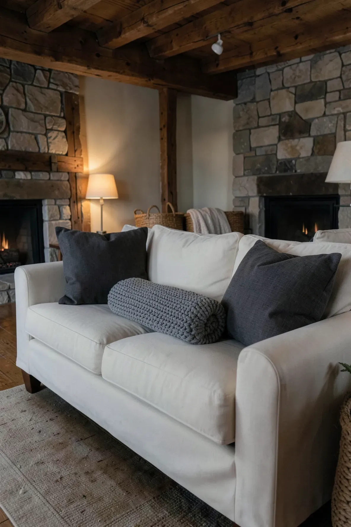 A deep cream sofa with two charcoal square pillows and a long chunky-knit lumbar cushion.