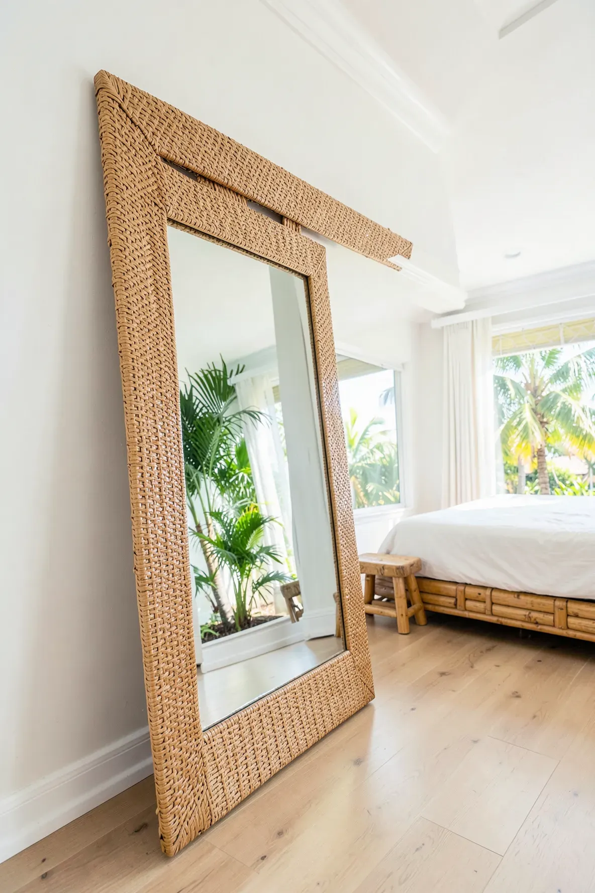 A large full-length mirror with a woven rattan frame leaning against a bedroom wall.