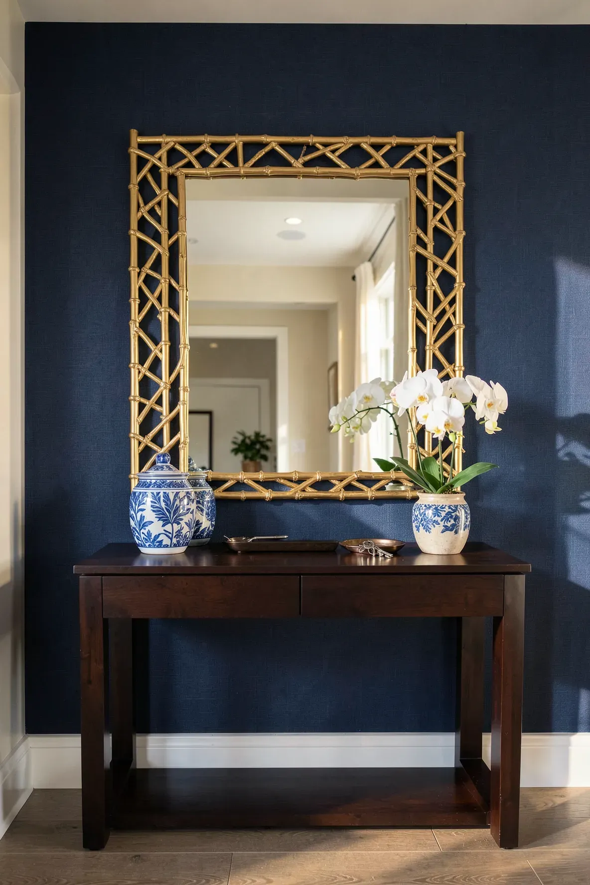 A gold leaf bamboo-style mirror hanging above a console table against navy blue walls.