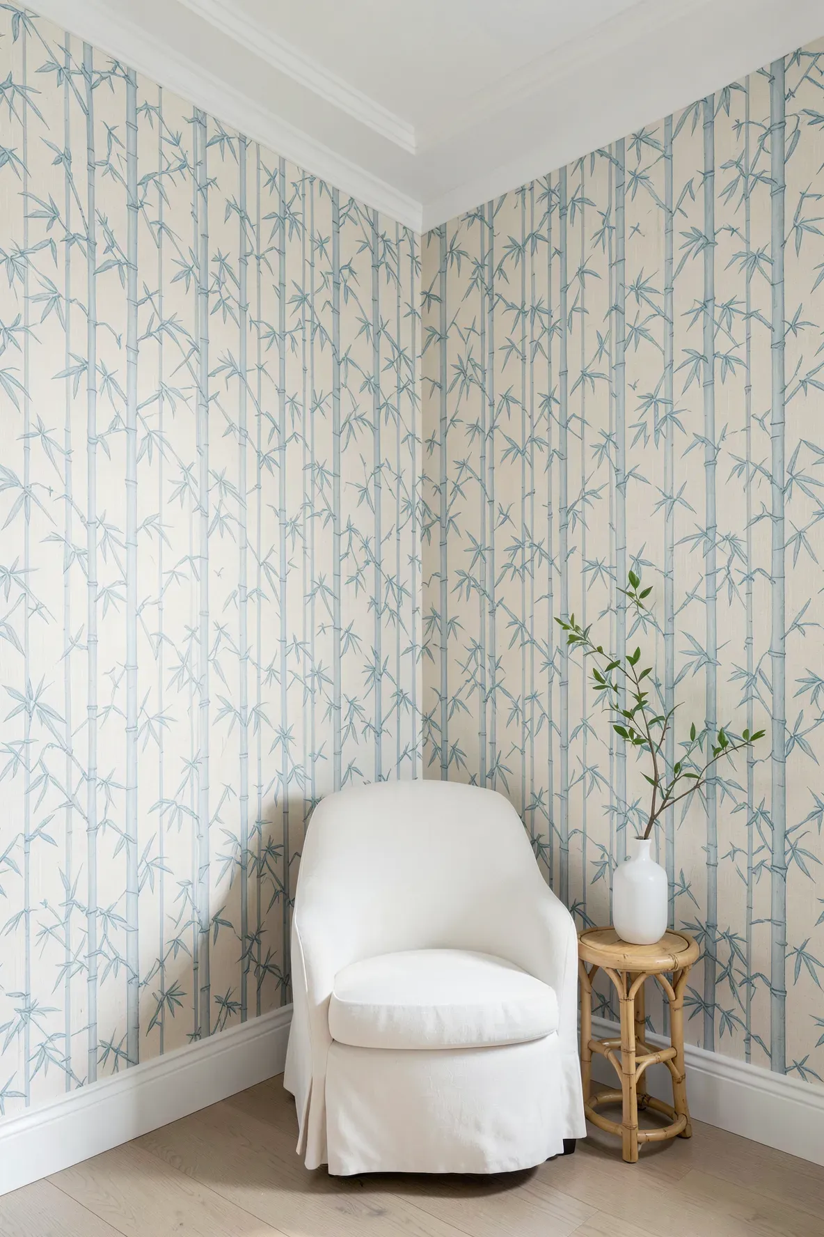 A room with soft blue bamboo patterned wallpaper and a white armchair in a peaceful corner.