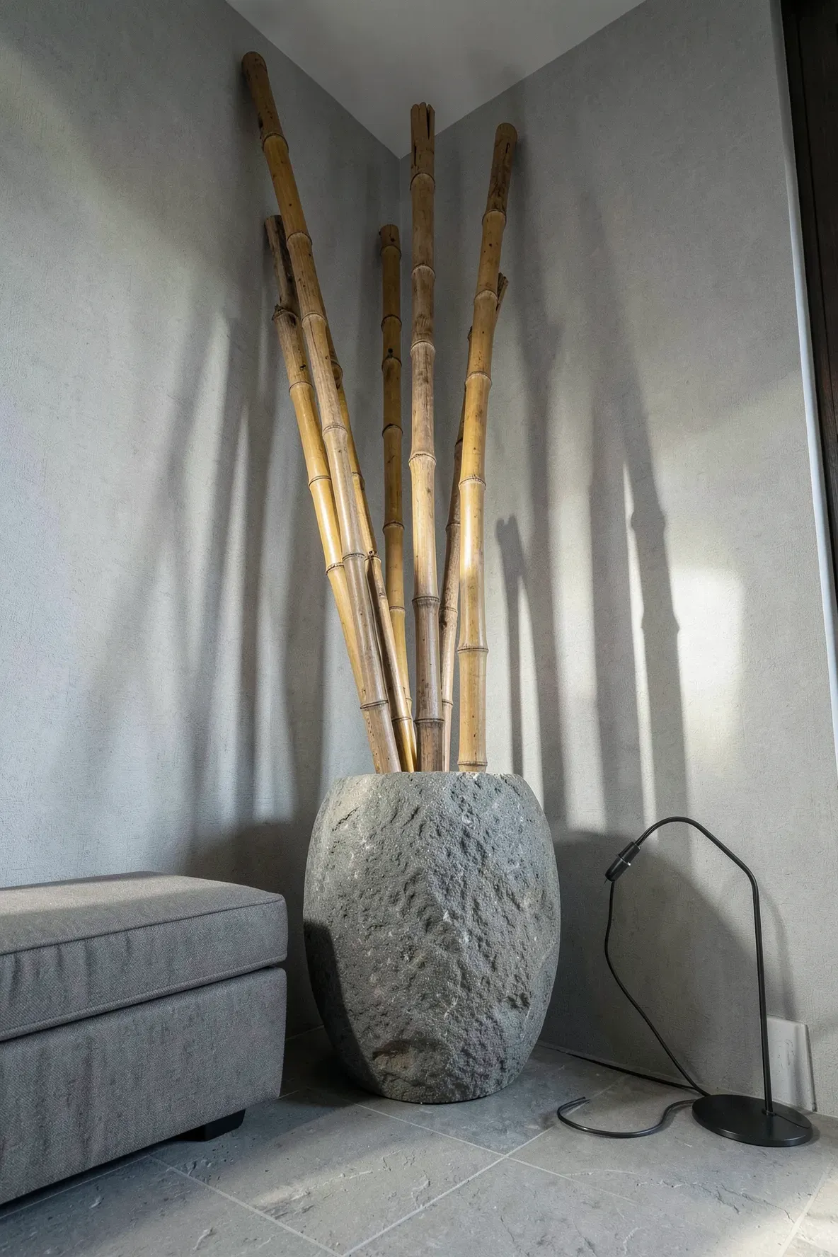 Tall bamboo stalks in a textured grey stone vase placed in a minimalist bedroom corner.