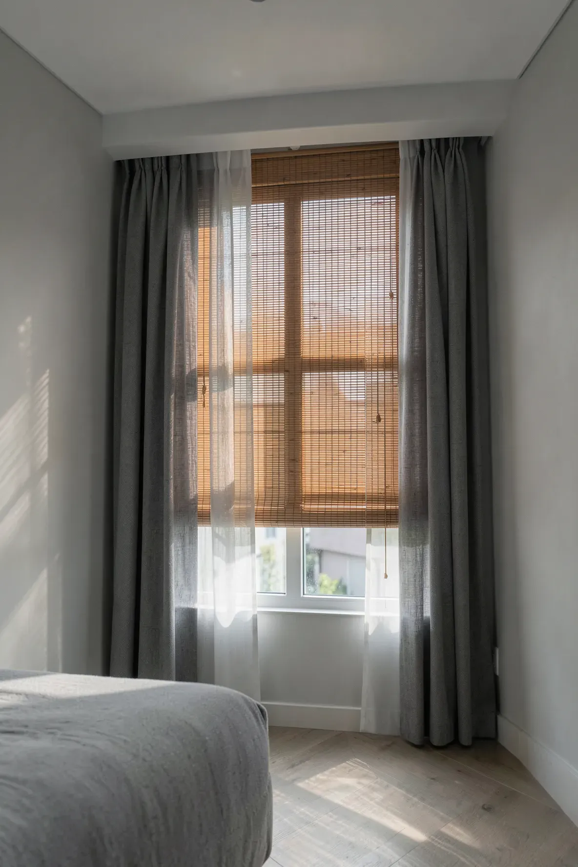 Layered sheer grey curtains and bamboo Roman blinds on a window in a modern Zen bedroom.