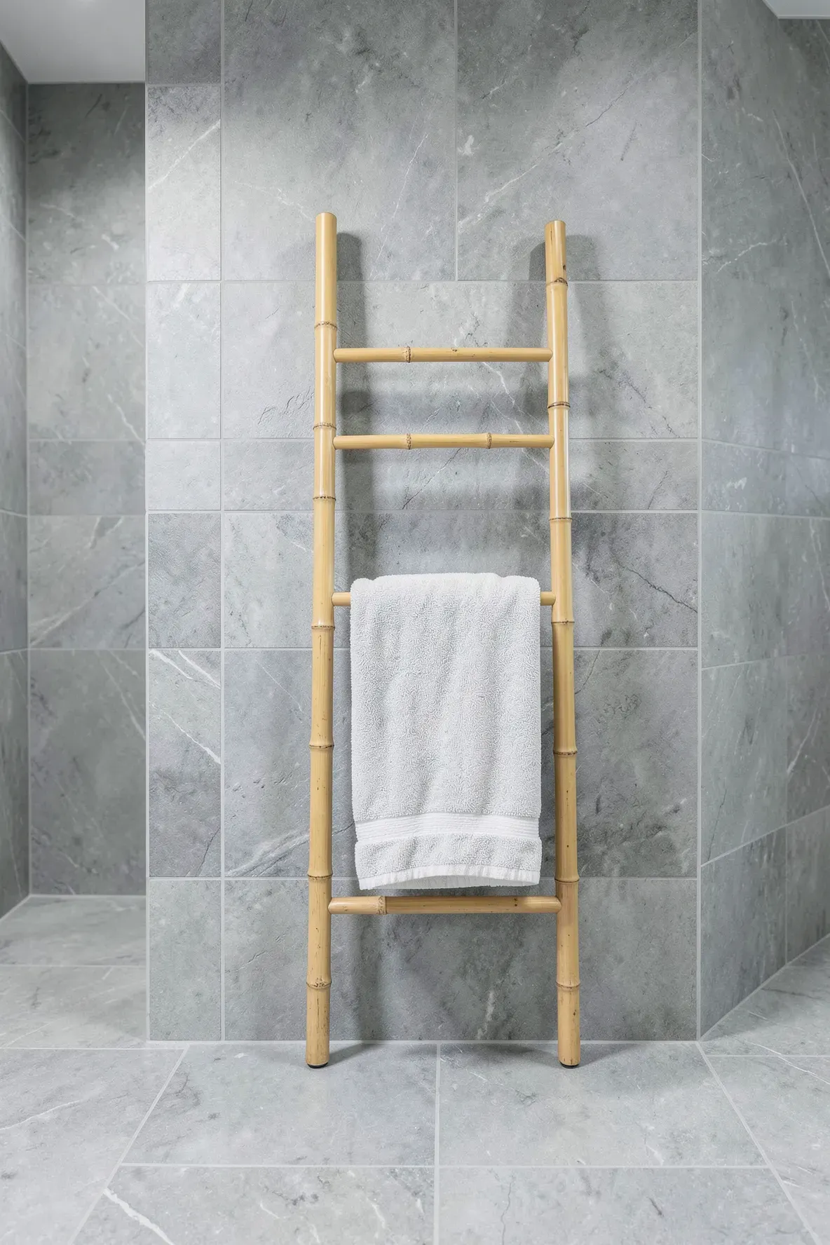 A bamboo ladder towel rack leaning against a grey tiled wall in a minimalist en suite bathroom.