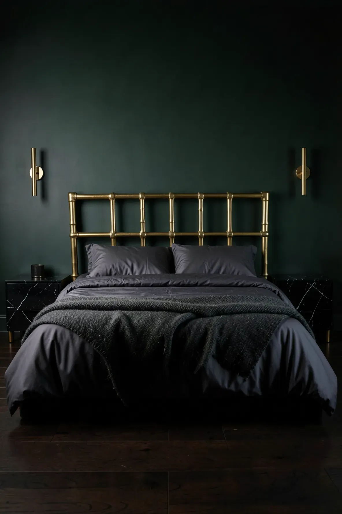 A polished brass faux bamboo headboard against a dark forest green wall in a moody, luxurious bedroom.