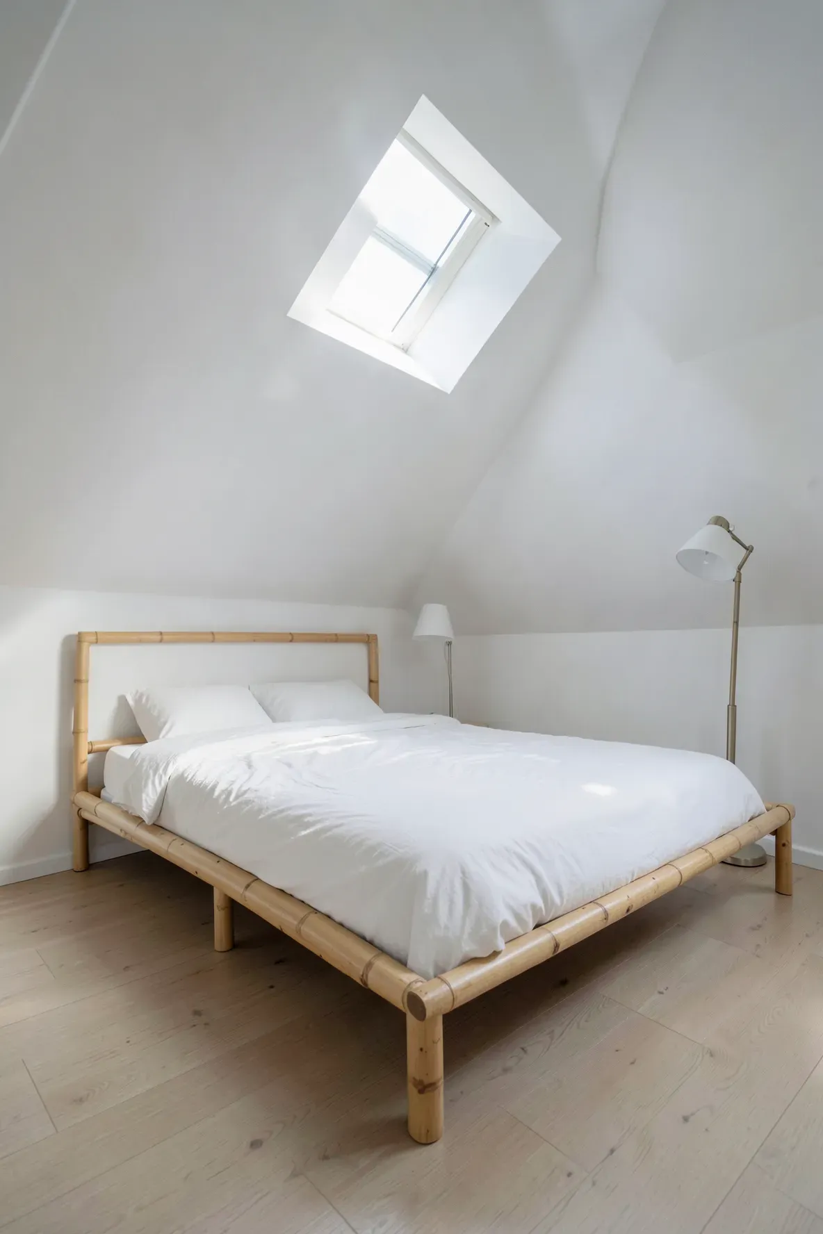 A minimalist attic bedroom with a low-profile bamboo bed frame and airy skylight lighting.