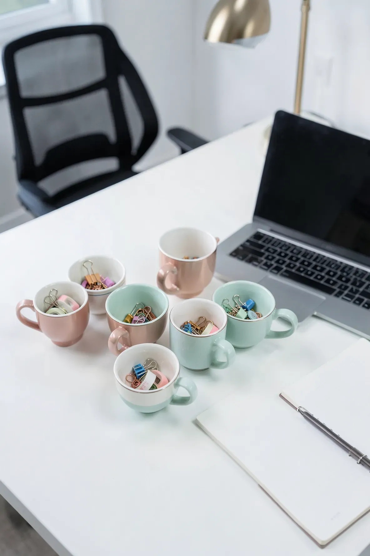Vintage teacups used as desk organizers for paperclips and stationery in a modern office.