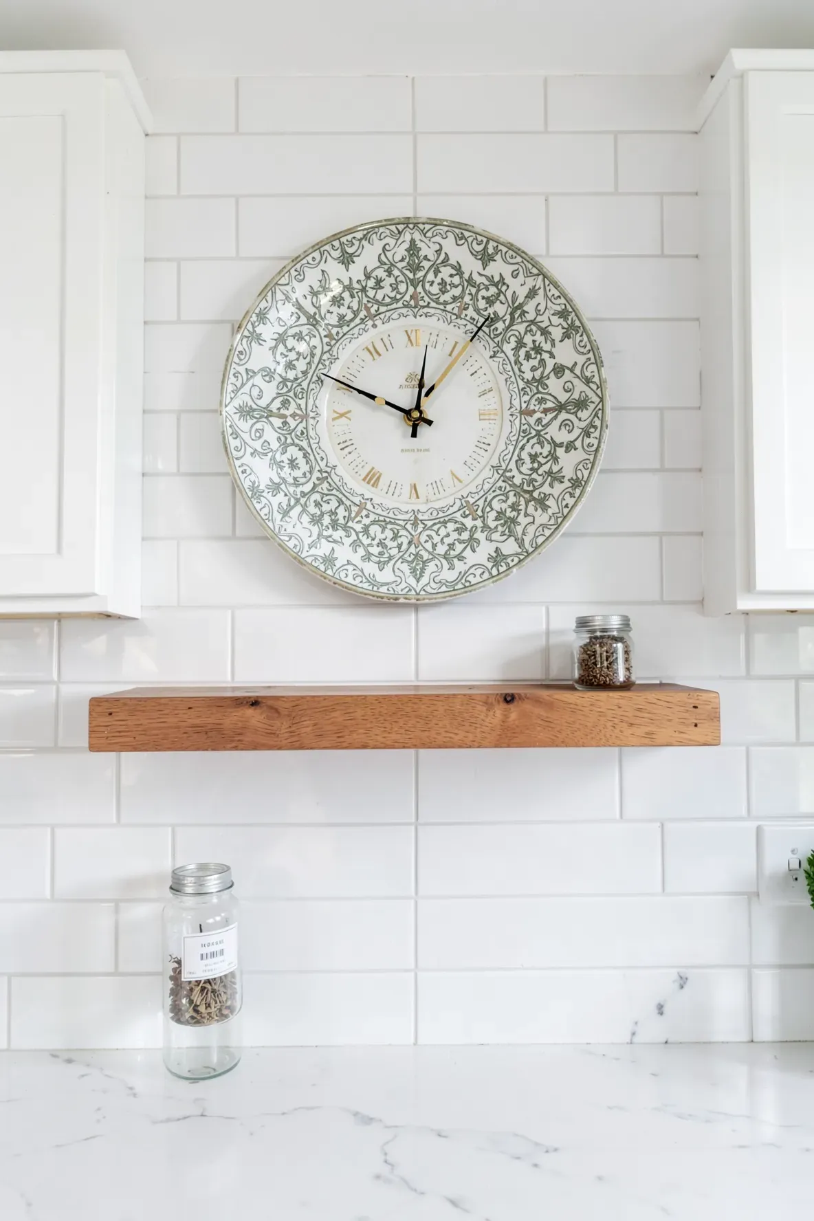 A decorative ceramic saucer converted into a wall clock, hanging on a white tiled kitchen wall.