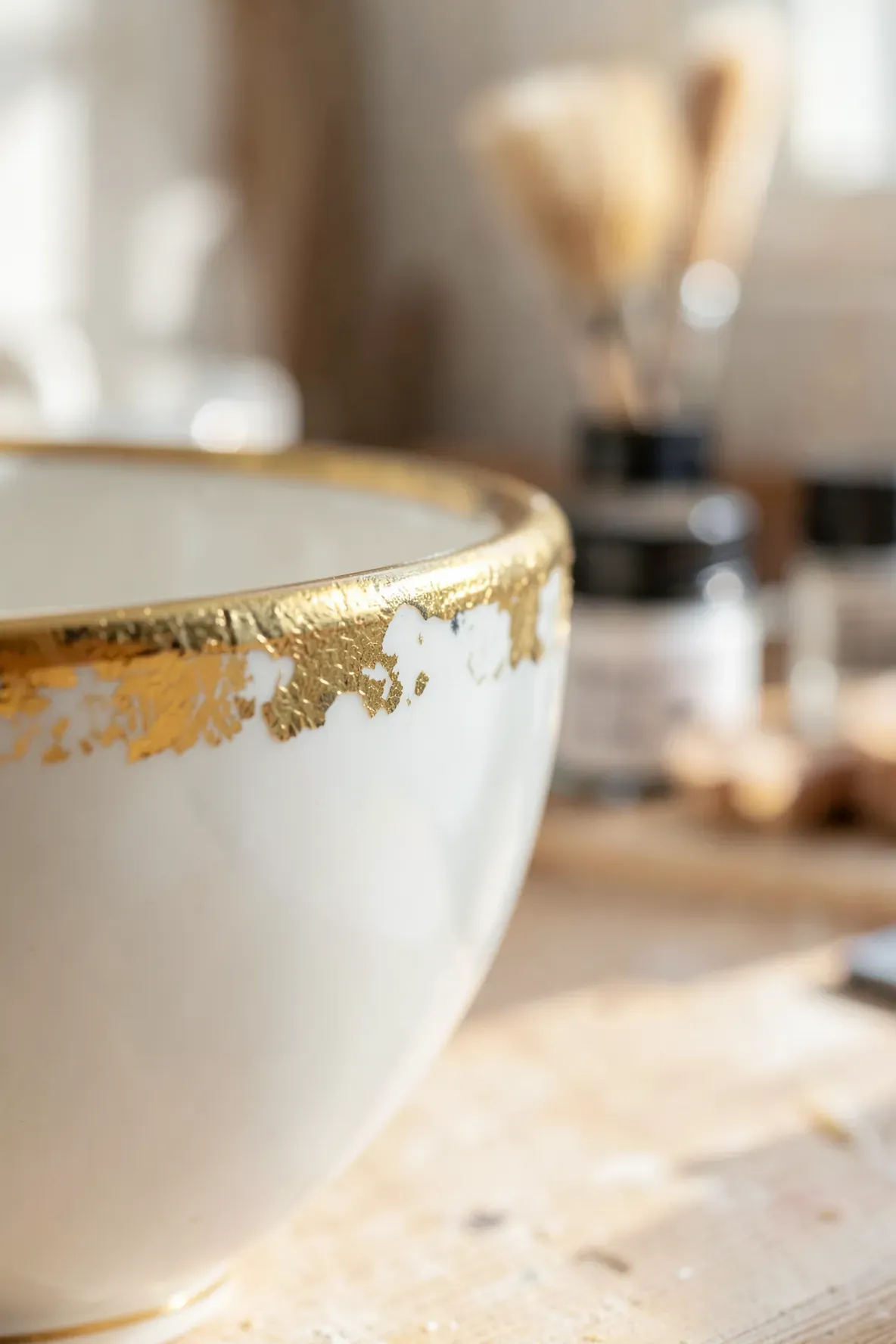 Close-up of a white tea cup with a shimmering gold leaf rim on a wooden table.