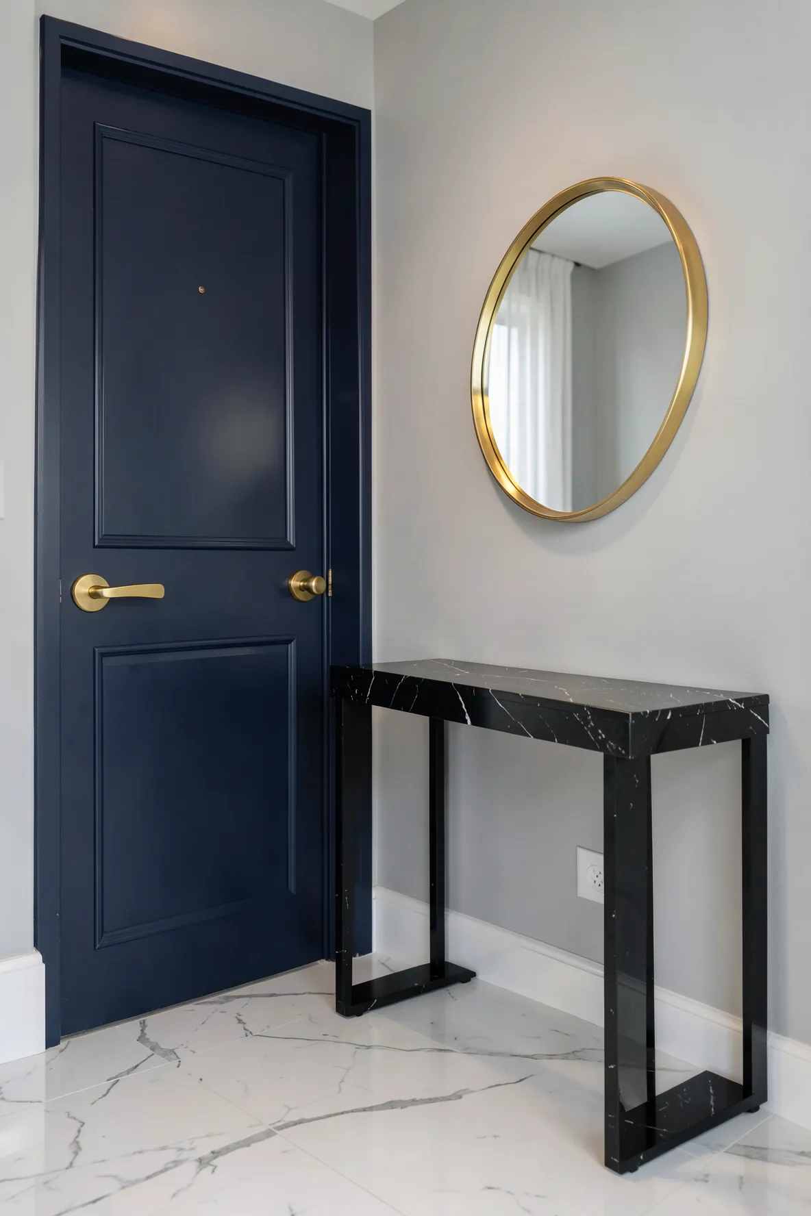 A polished entryway featuring a navy door and console table with matching brushed gold hardware.
