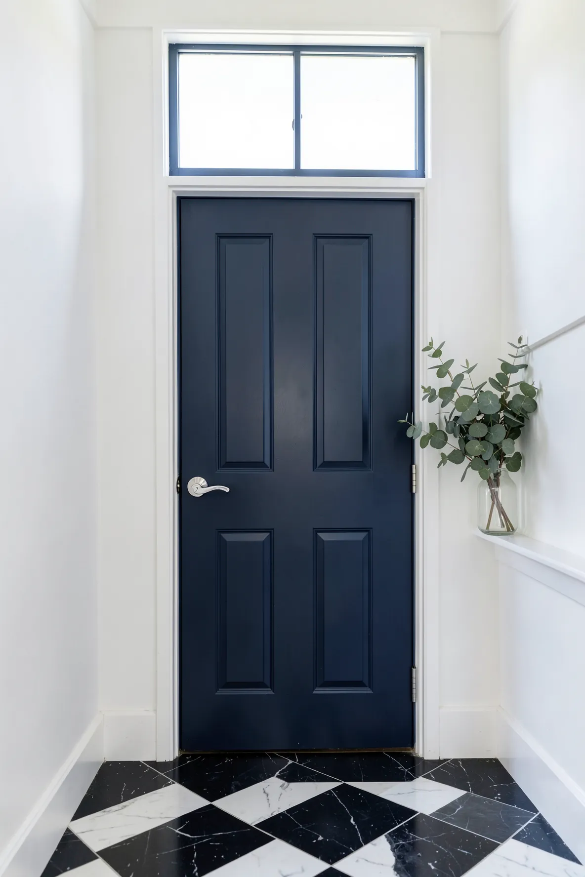 A navy blue painted interior front door contrasting against white walls and checkered floors.