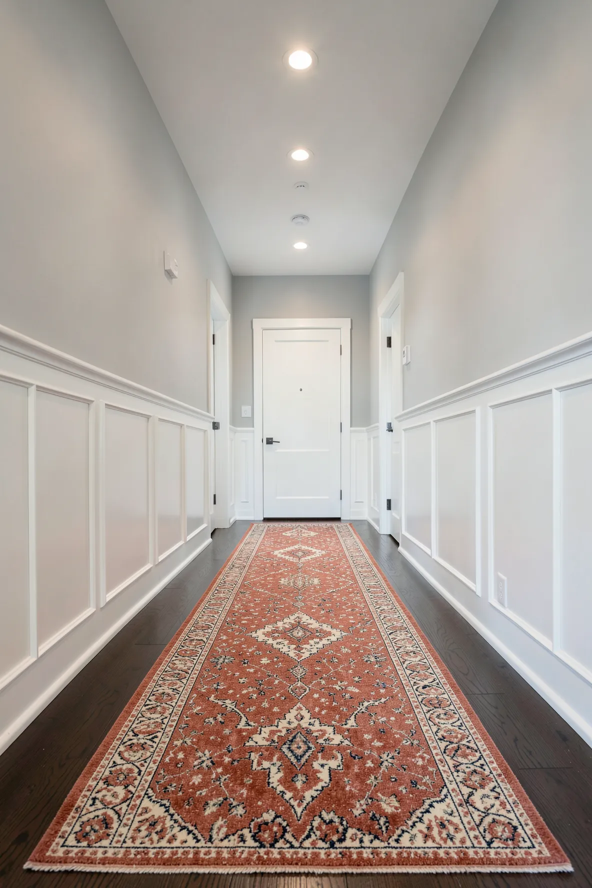 A long patterned wool runner rug extending down a bright hallway with dark wood floors.