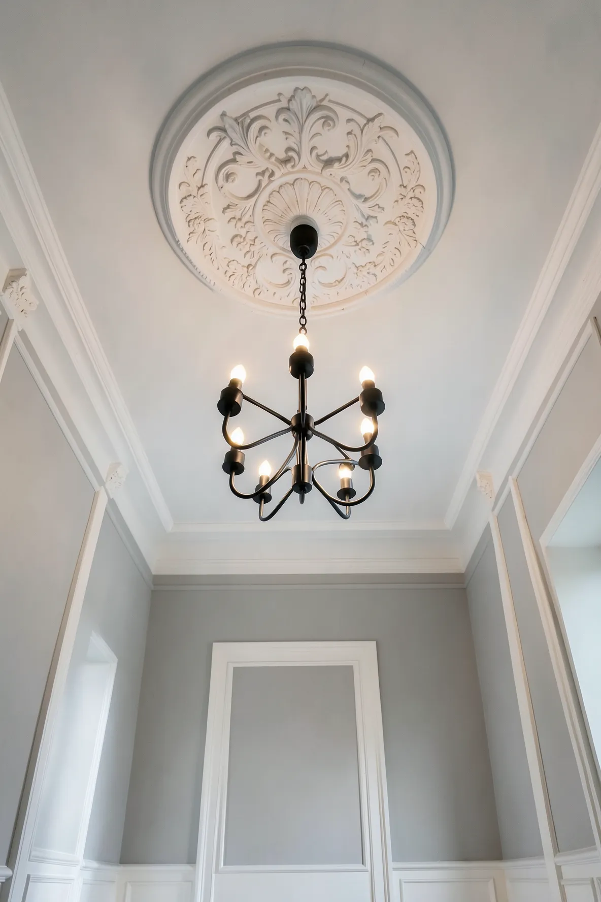 An ornate white ceiling medallion surrounding a modern black chandelier in a grand foyer.