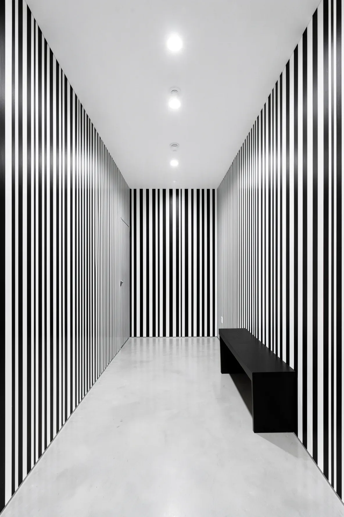 A narrow modern hallway with vertical black and white striped wallpaper and minimalist decor.