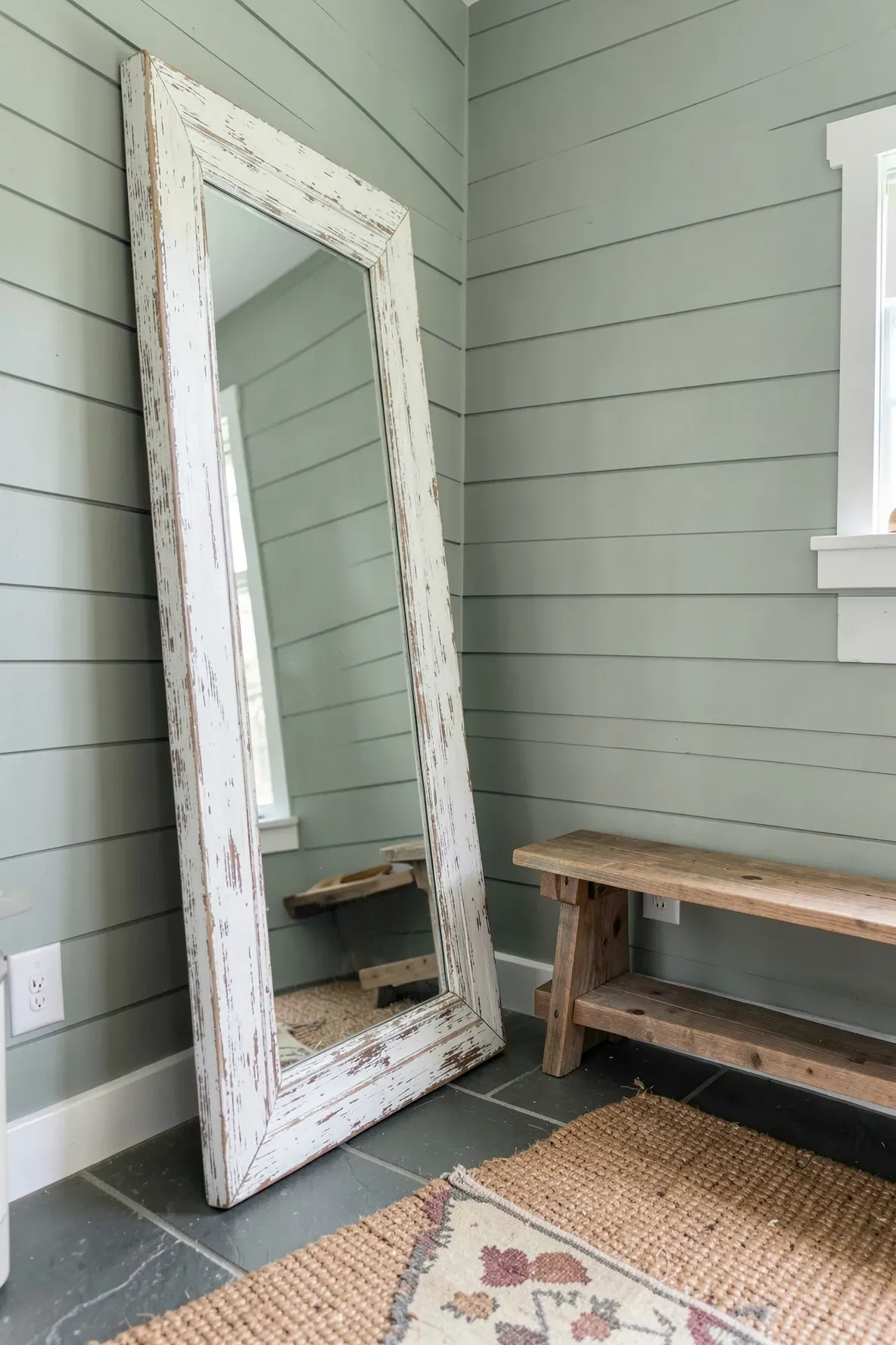 A rustic white-washed wooden full-length mirror leaning against a sage green wall.