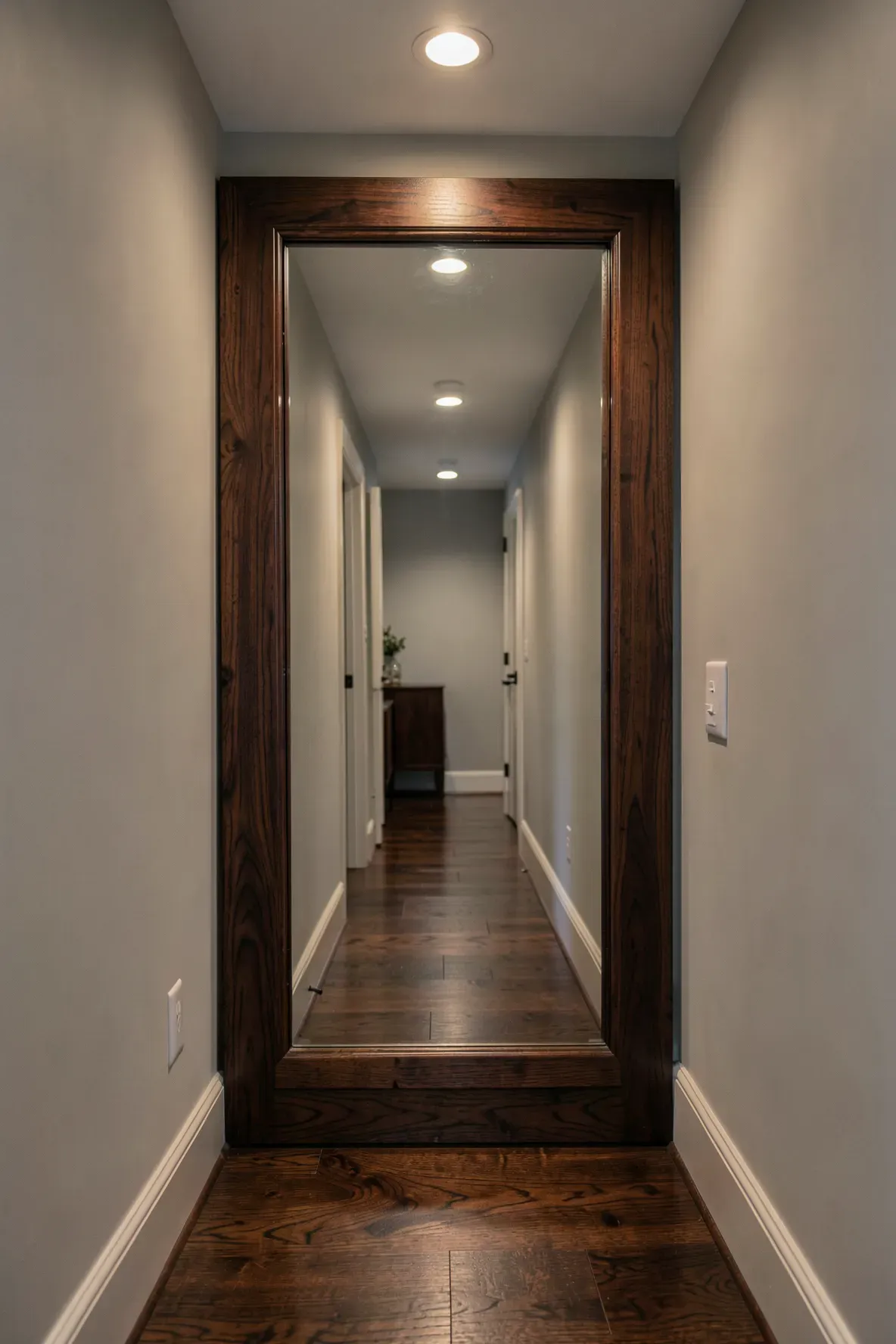 A dark walnut wood floor mirror tucked into a narrow, well-lit hallway alcove.